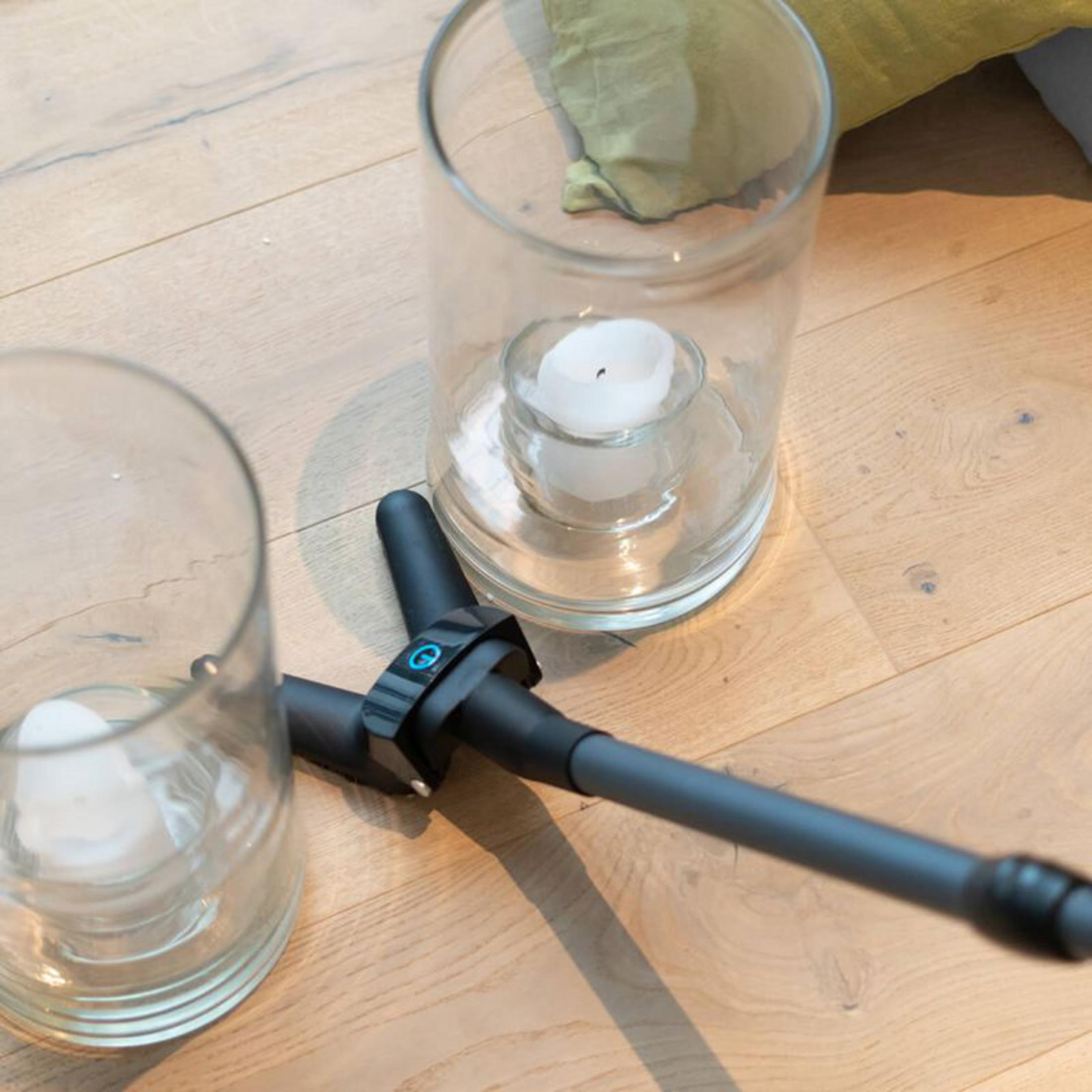 Zwei Glasbehälter mit weißen Kerzen auf Holzboden, daneben ein schwarzer Griff.
