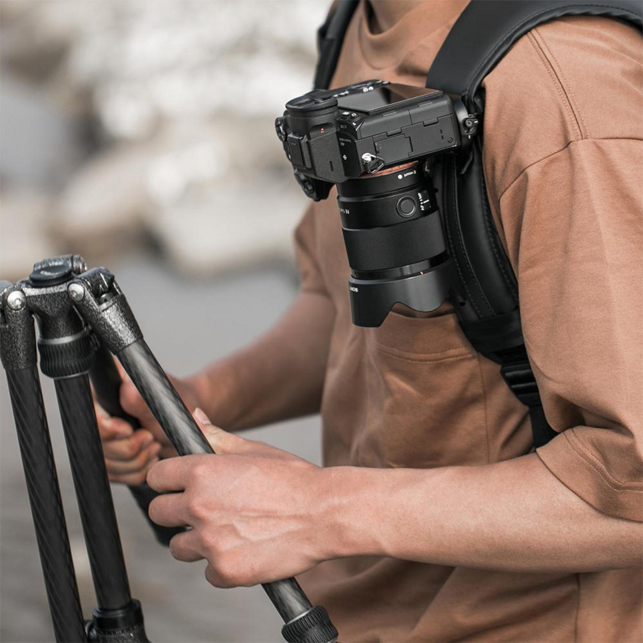 Zbliżenie na osobę z aparatem na plecach i statywem w dłoniach.