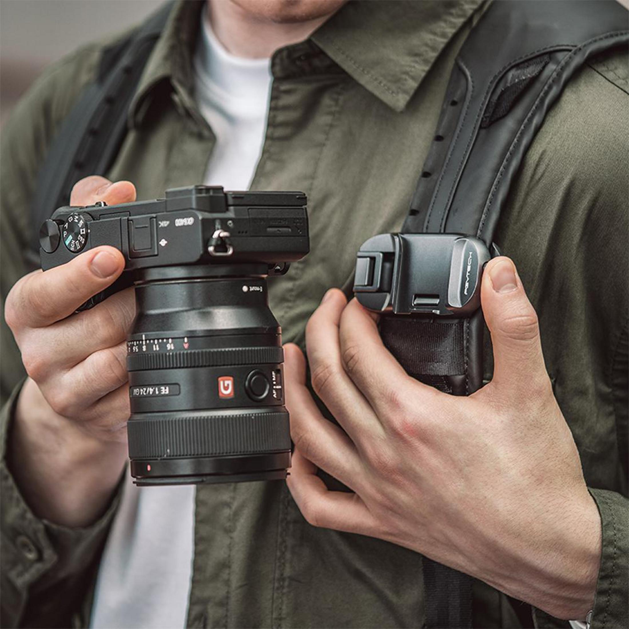 Osoba trzyma aparat z obiektywem i uchwytem na pasek.