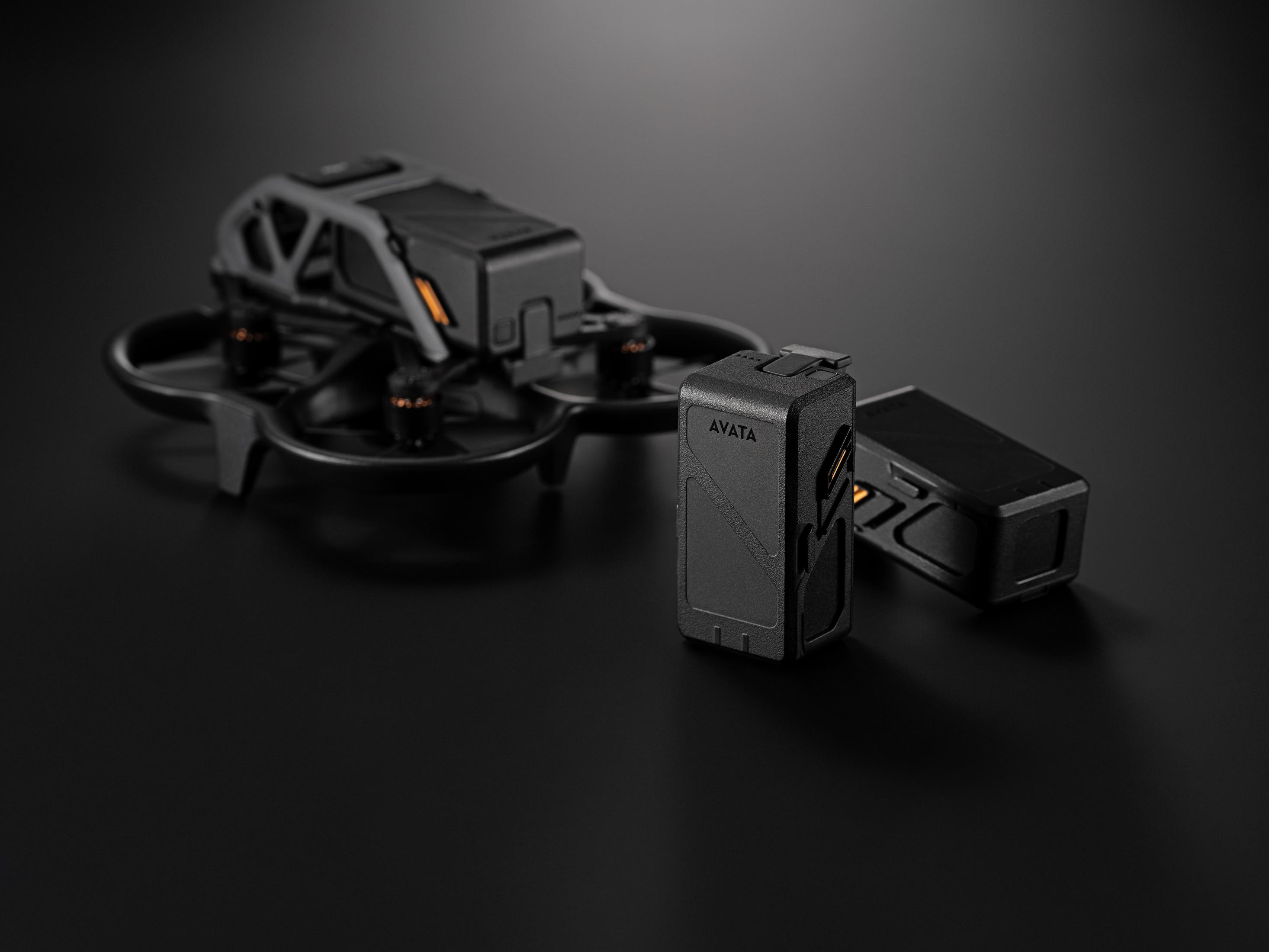 Un paquete de baterías de dron negro está en primer plano, un dron detrás.