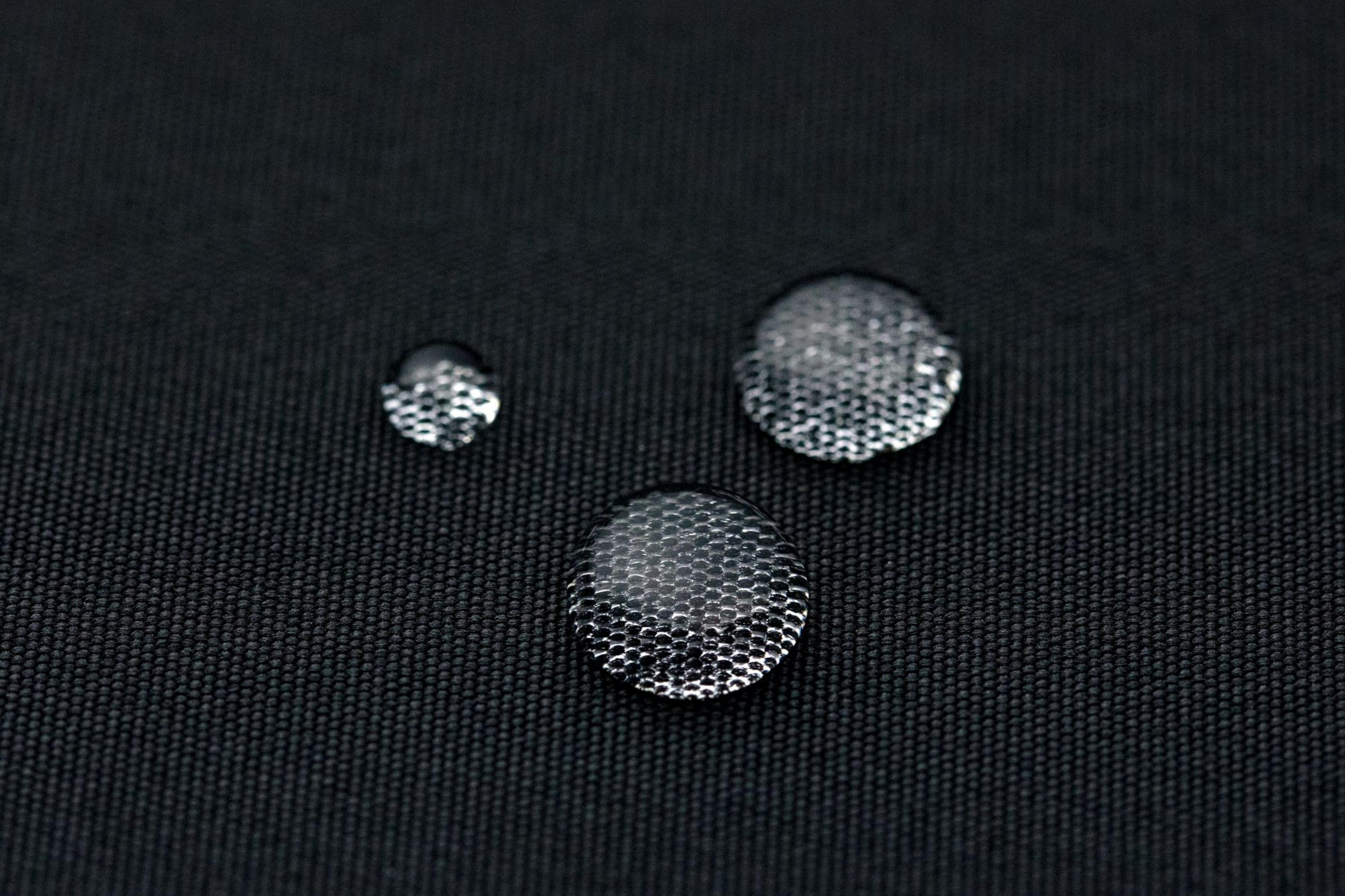 Tre gocce d'acqua su tessuto nero con texture a nido d'ape.