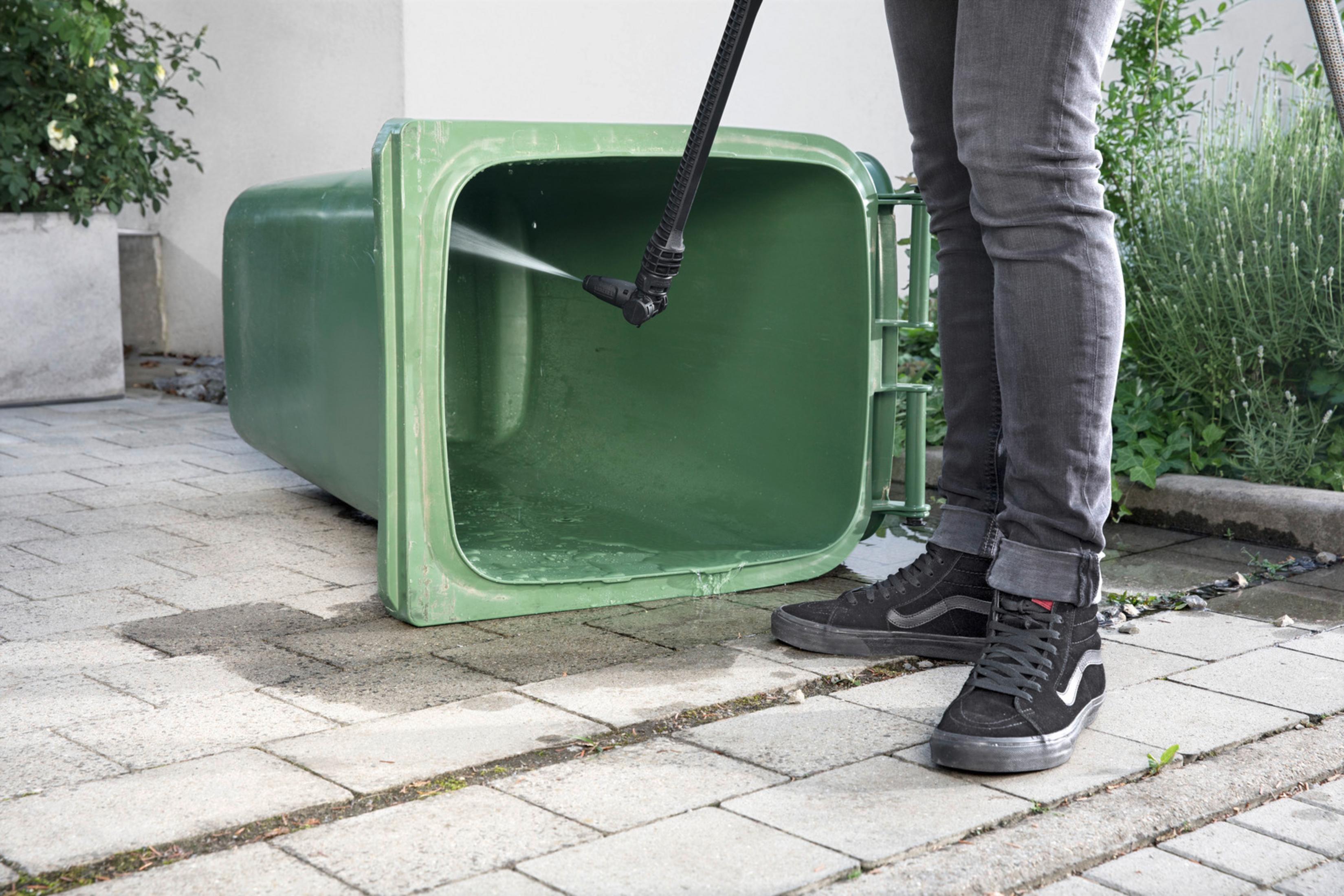Contenedor de basura verde limpiado con hidrolimpiadora. Persona en jeans.