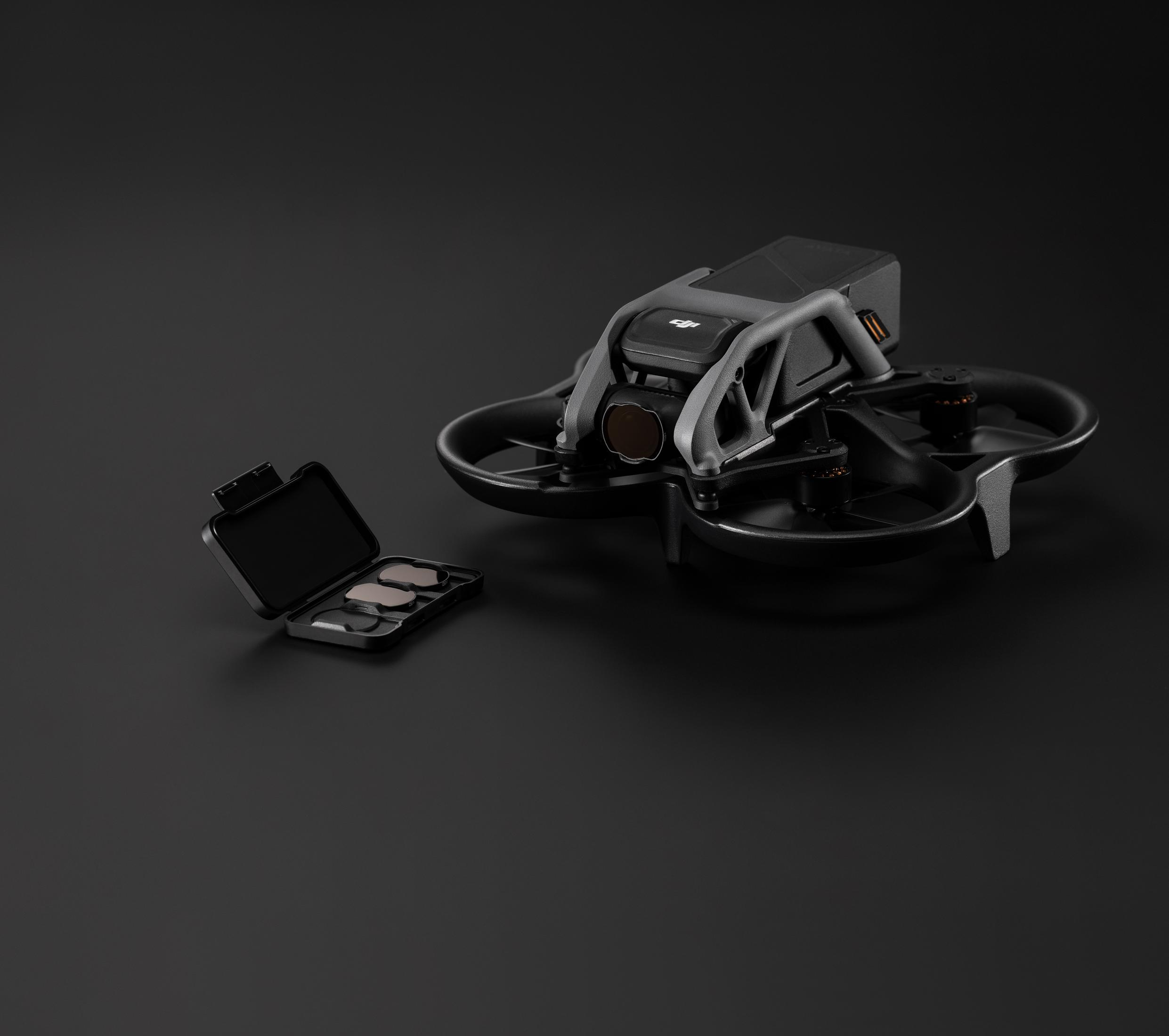 Un dron negro con cámara y una pequeña caja de filtros sobre fondo negro.