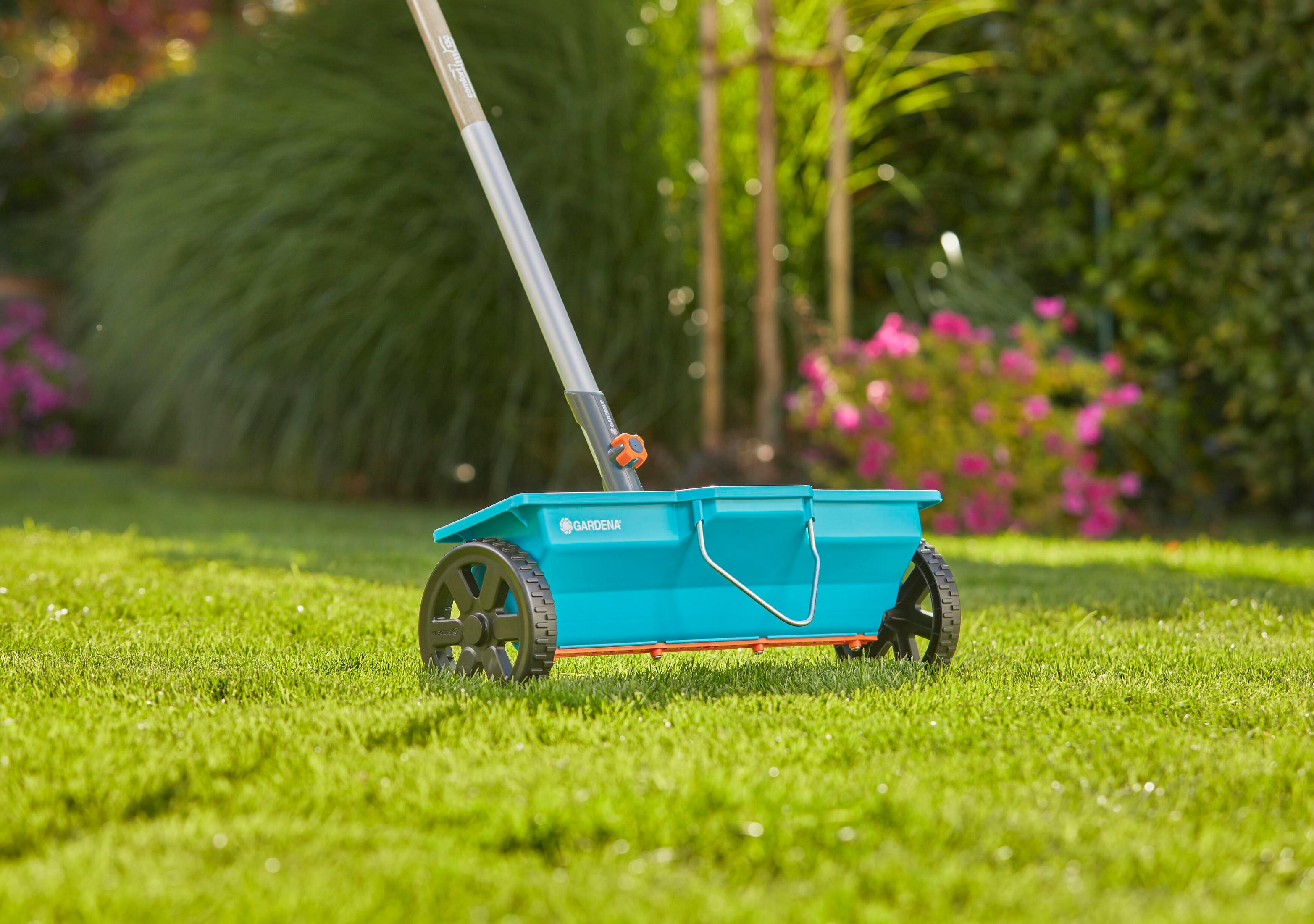 Un carrello spargisale blu con ruote e manico si trova sull'erba verde.