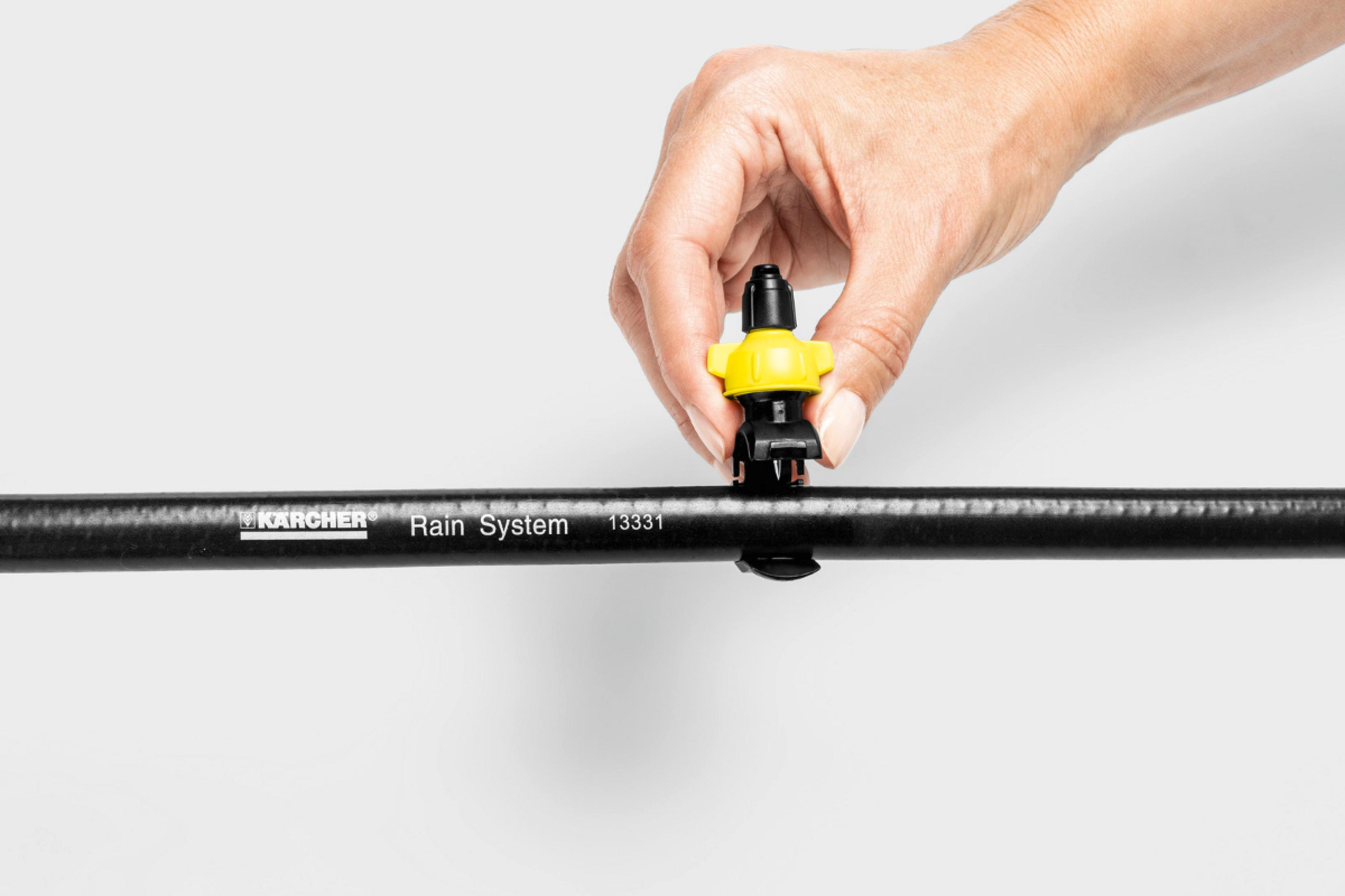 Eine Hand befestigt einen gelben und schwarzen Sprinkler an einem schwarzen Schlauch.