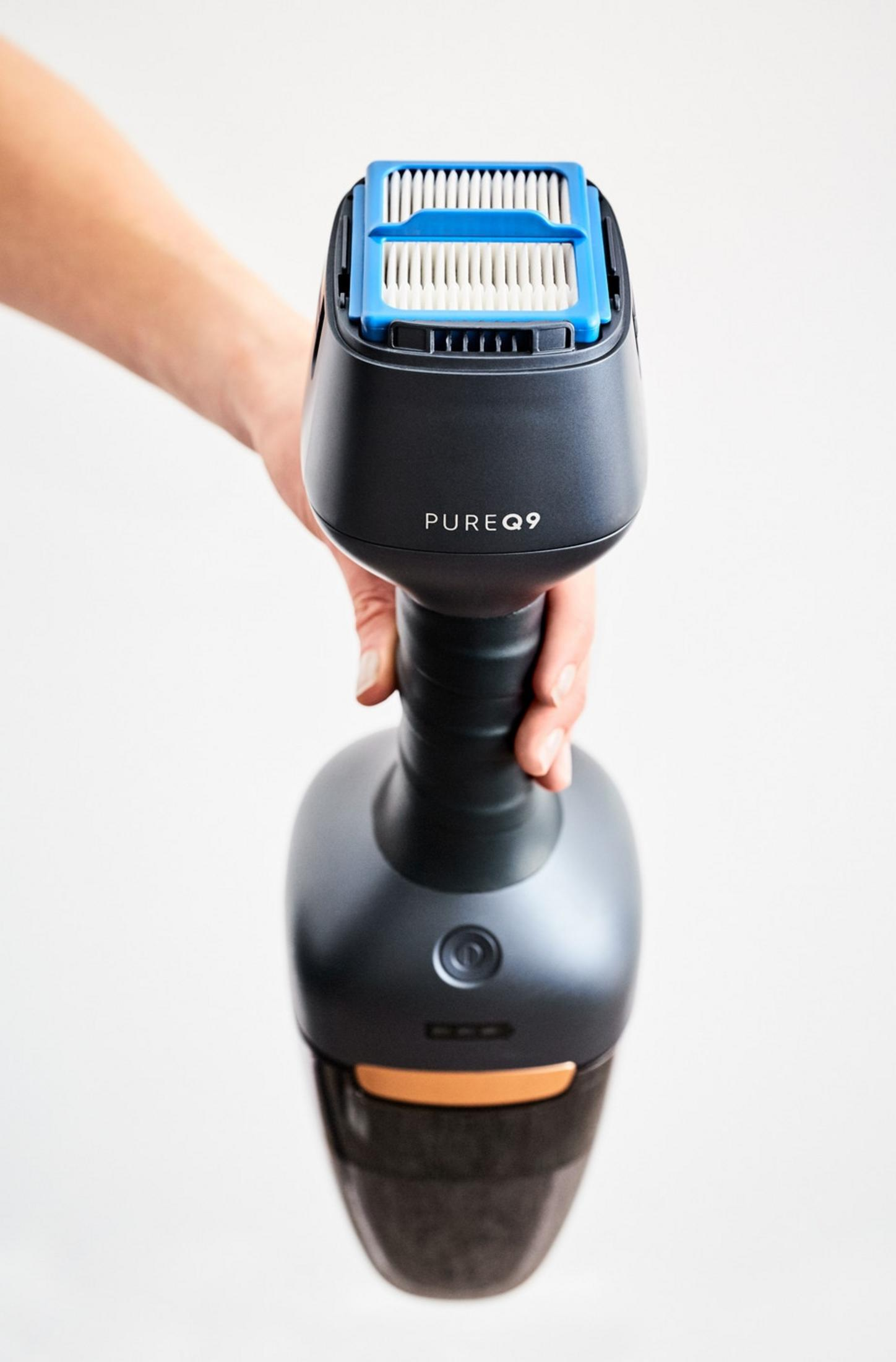 Une main tient un aspirateur gris foncé avec un filtre bleu et blanc sur le dessus.