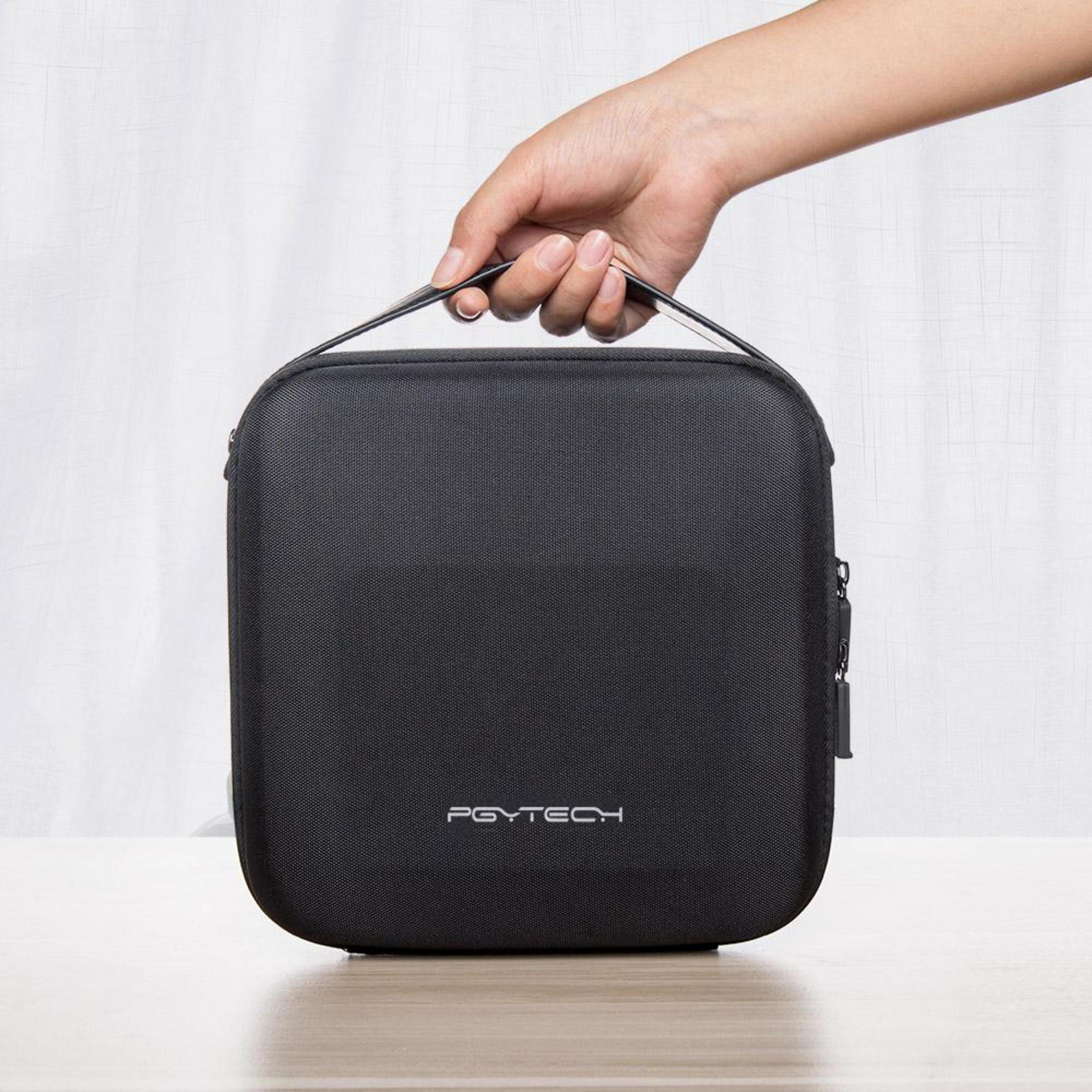 Una mano sujeta el asa de una bolsa negra PGYTECH sobre una mesa de madera.