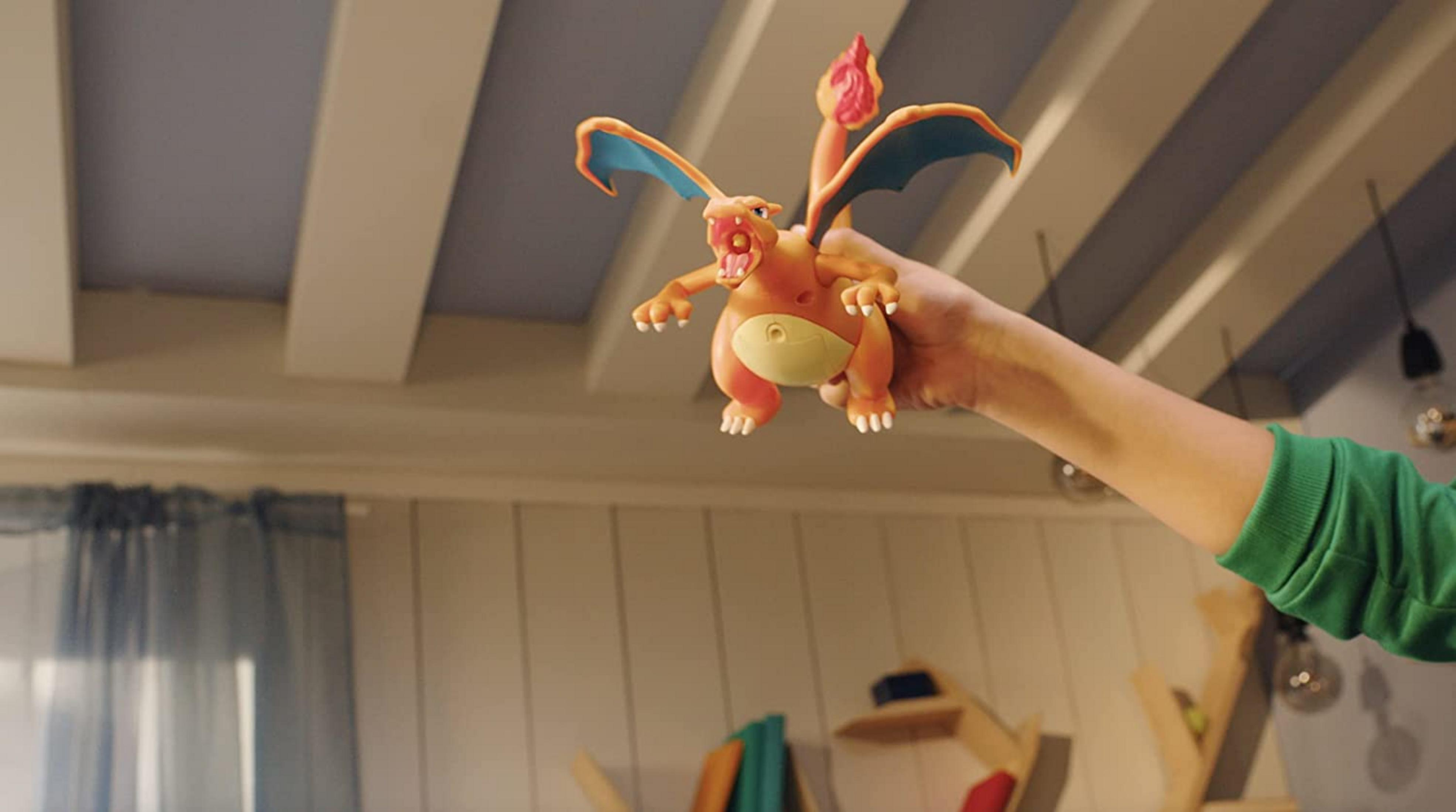 Eine orangefarbene Charizard-Figur mit blauen Flügeln wird von einer Hand gehalten.