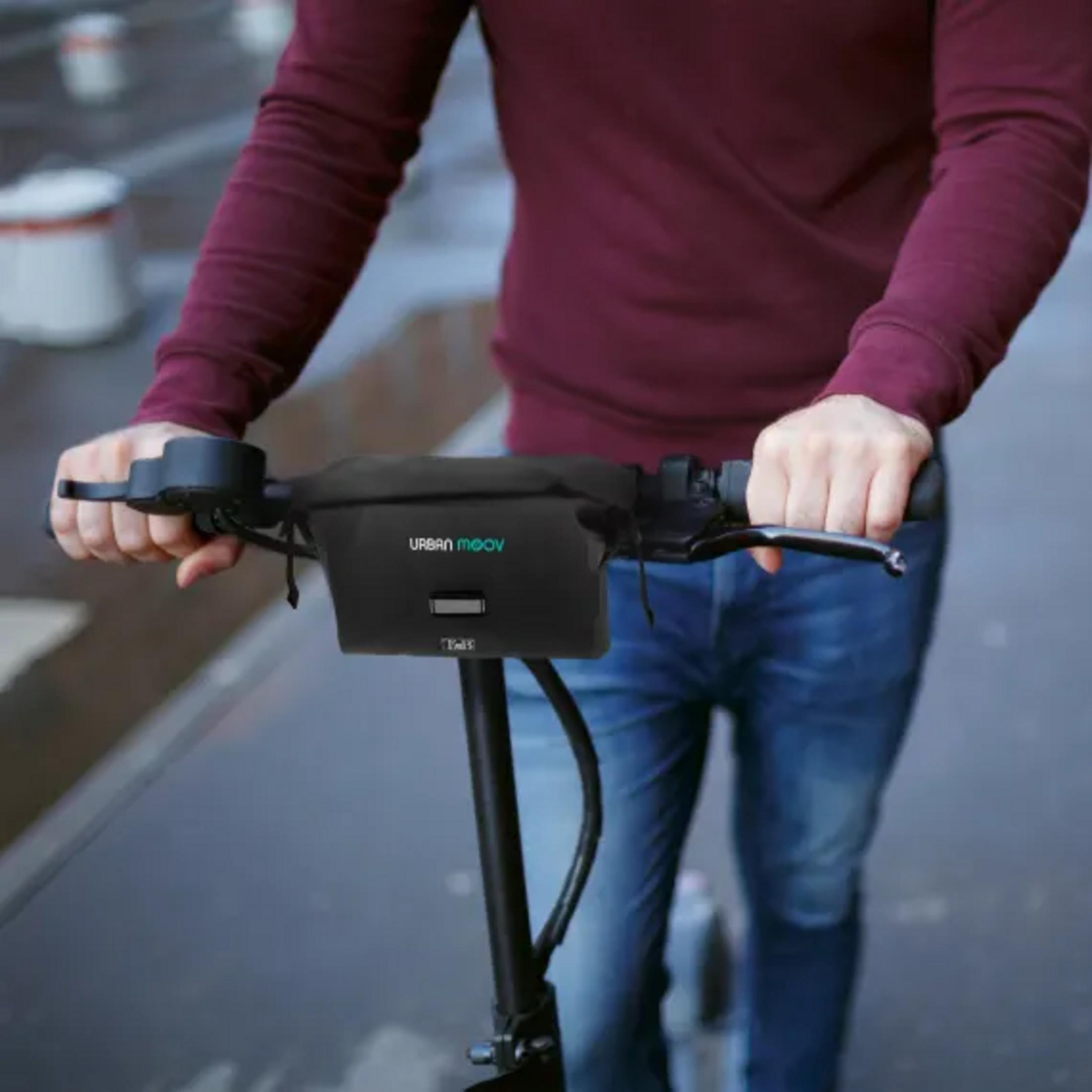 Person in rotem Hemd und blauer Jeans fährt Elektroroller, hält Lenker.