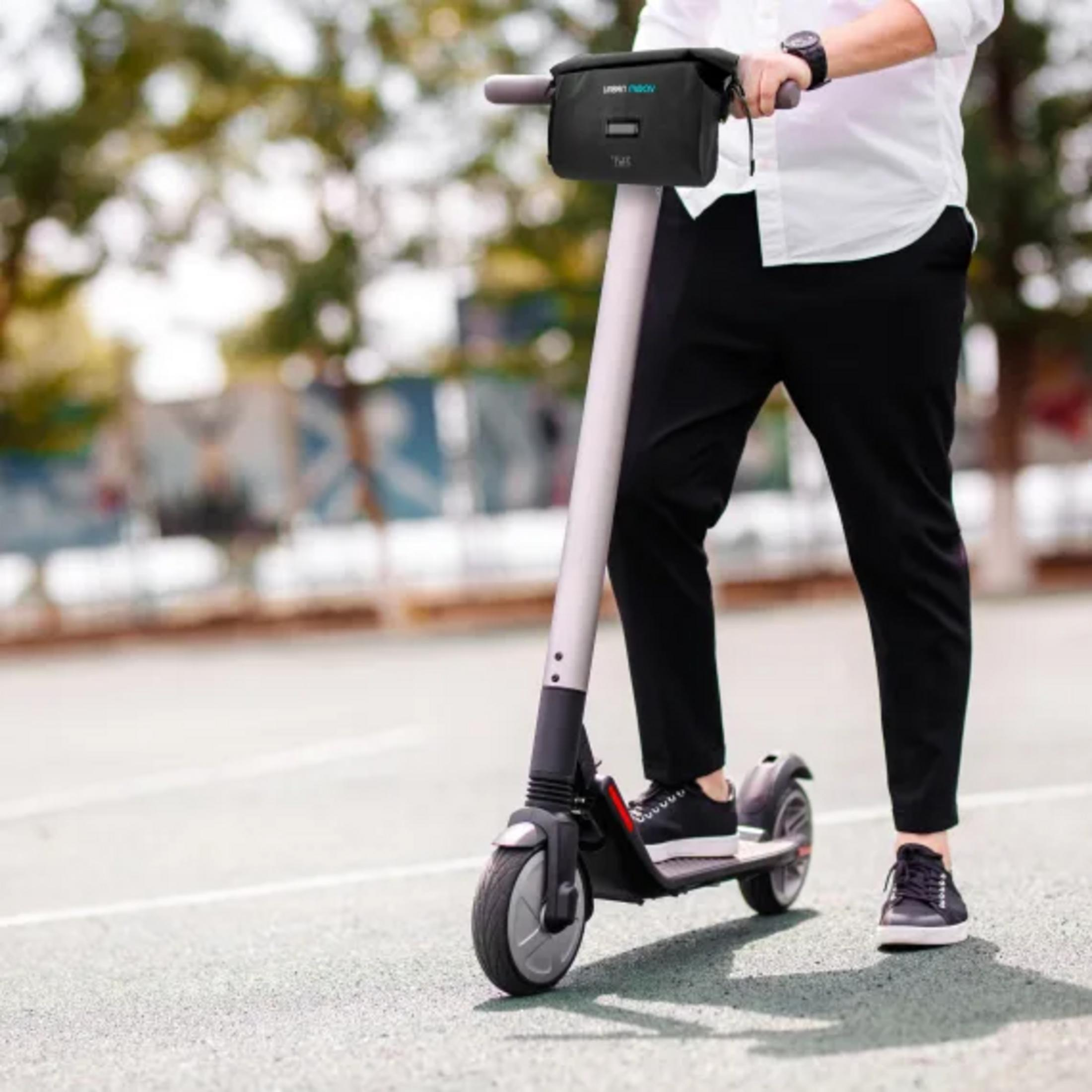Person mit weißem Hemd und schwarzer Hose fährt E-Scooter mit Lenkertasche.