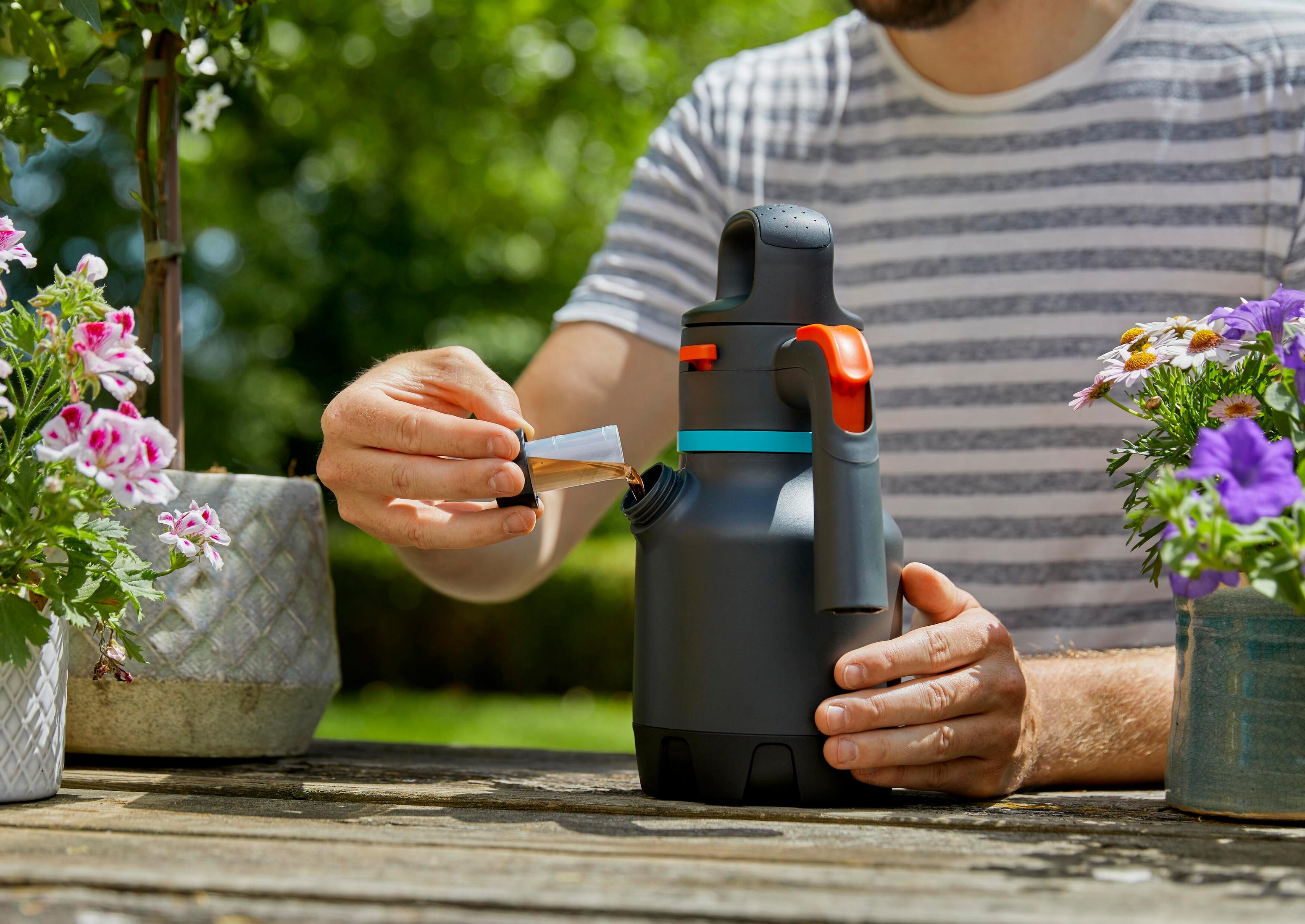 Mann füllt Flüssigkeit aus Messbecher in dunkelgraue Sprühflasche neben Blumen.