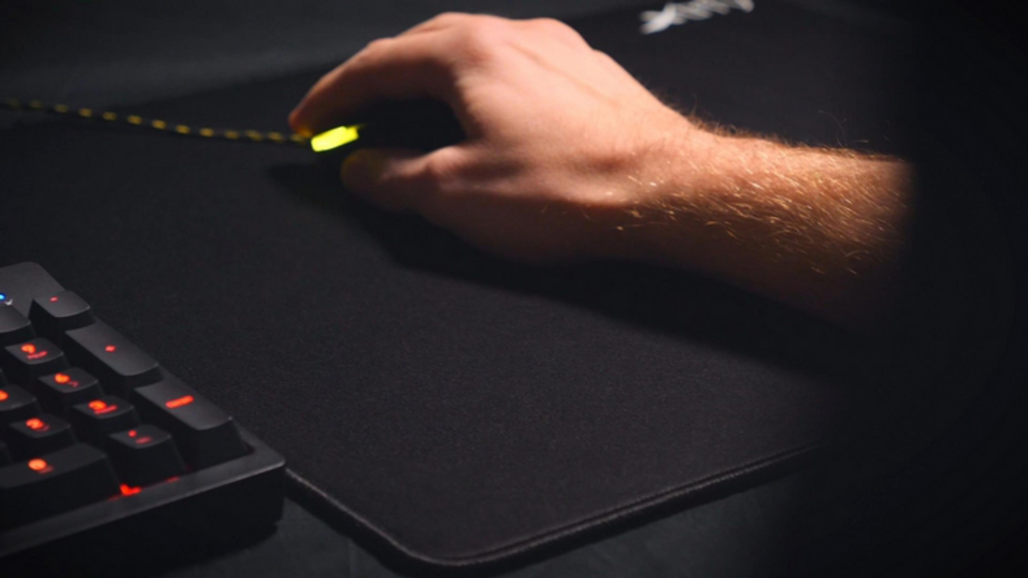 Main actionne une souris gamer jaune lumineuse sur tapis noir, clavier au premier plan.