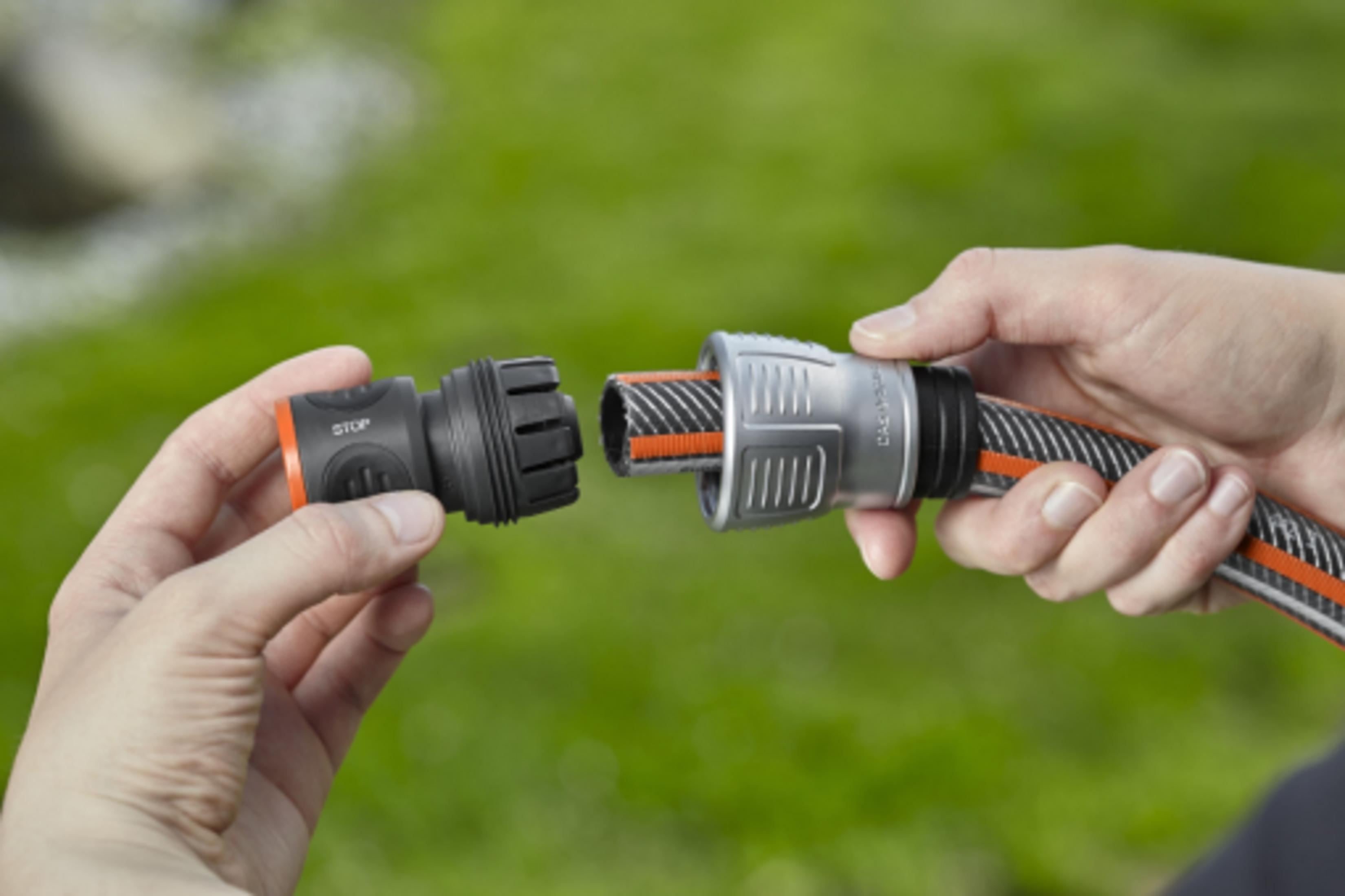 Mani che collegano un tubo da giardino a un connettore di arresto.