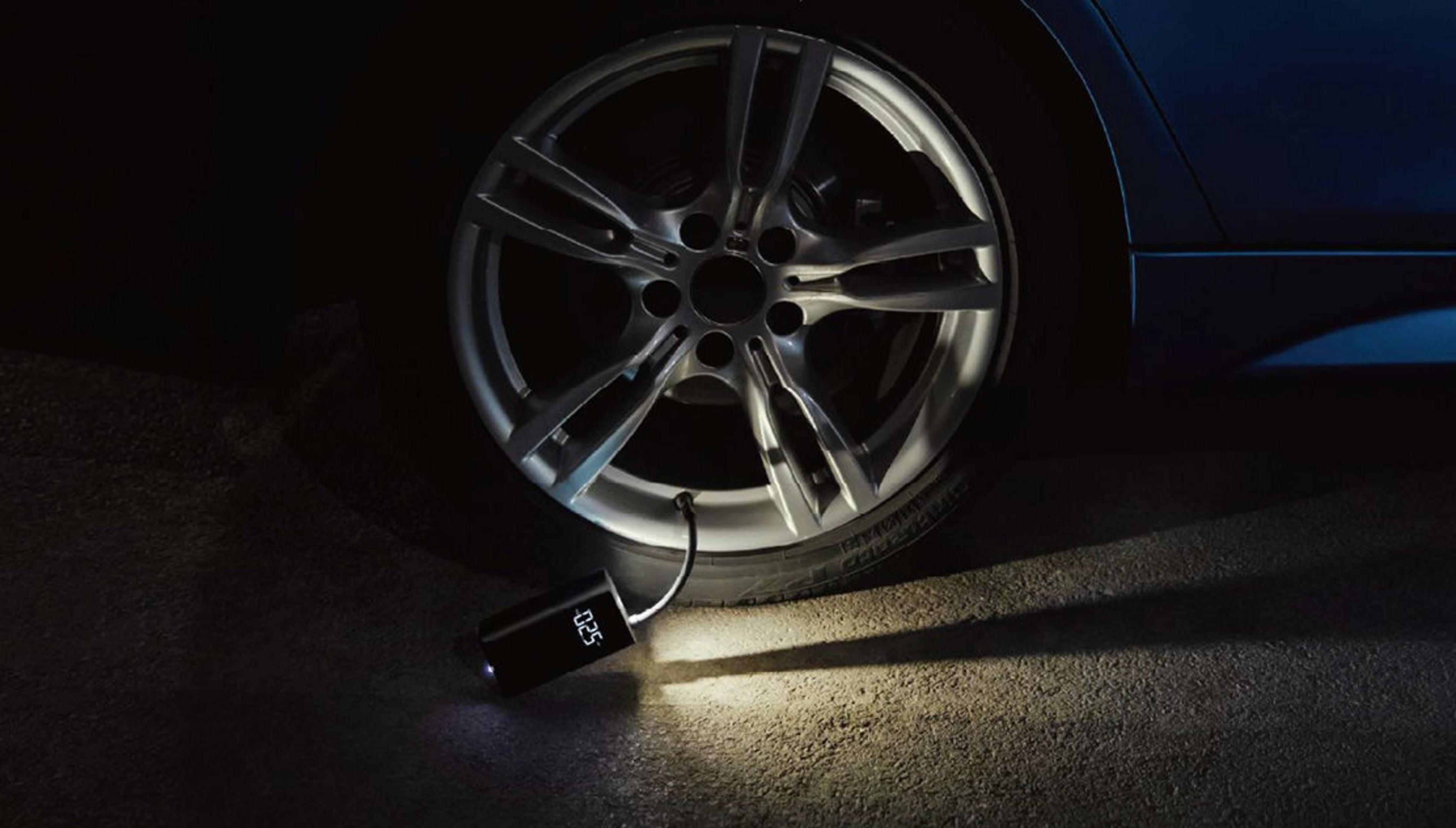 Un inflador de neumáticos portátil con pantalla junto a la rueda de un coche.