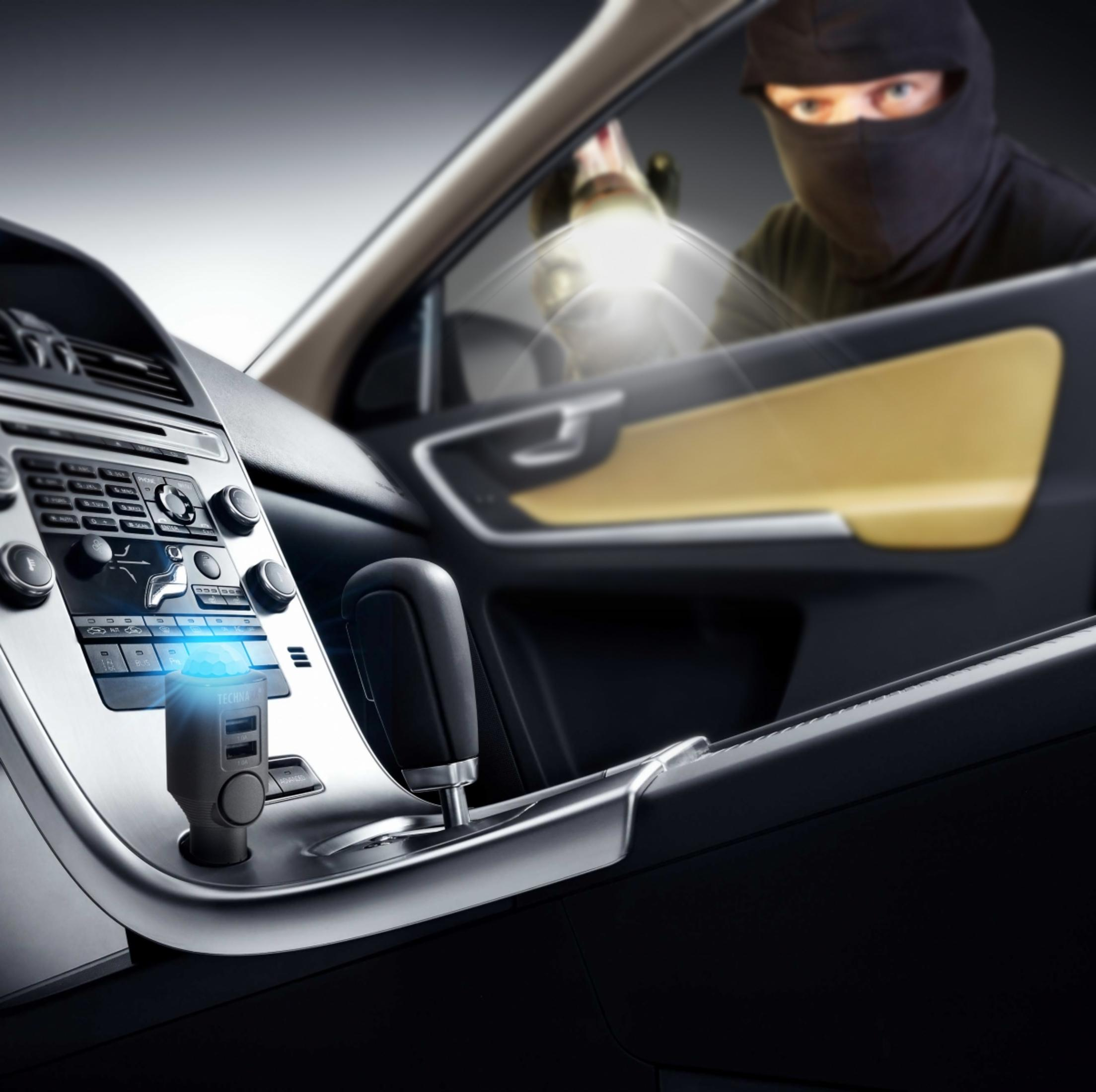 Ein maskierter Einbrecher leuchtet mit einer Taschenlampe in ein Auto. Innen ist ein USB-Ladegerät eingesteckt.