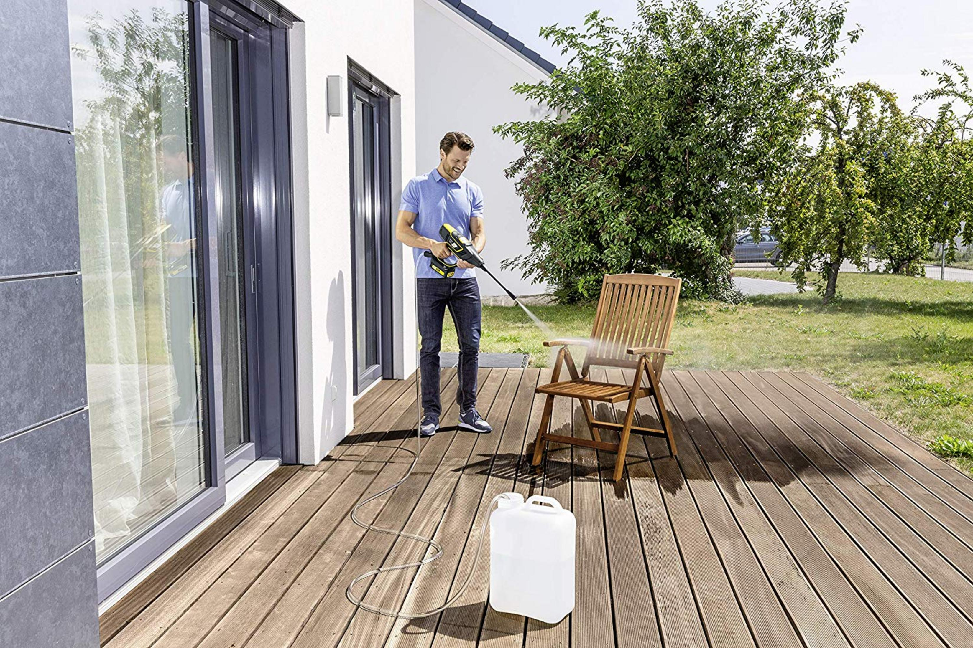 Un hombre usa una hidrolavadora para limpiar una silla de madera en una terraza.
