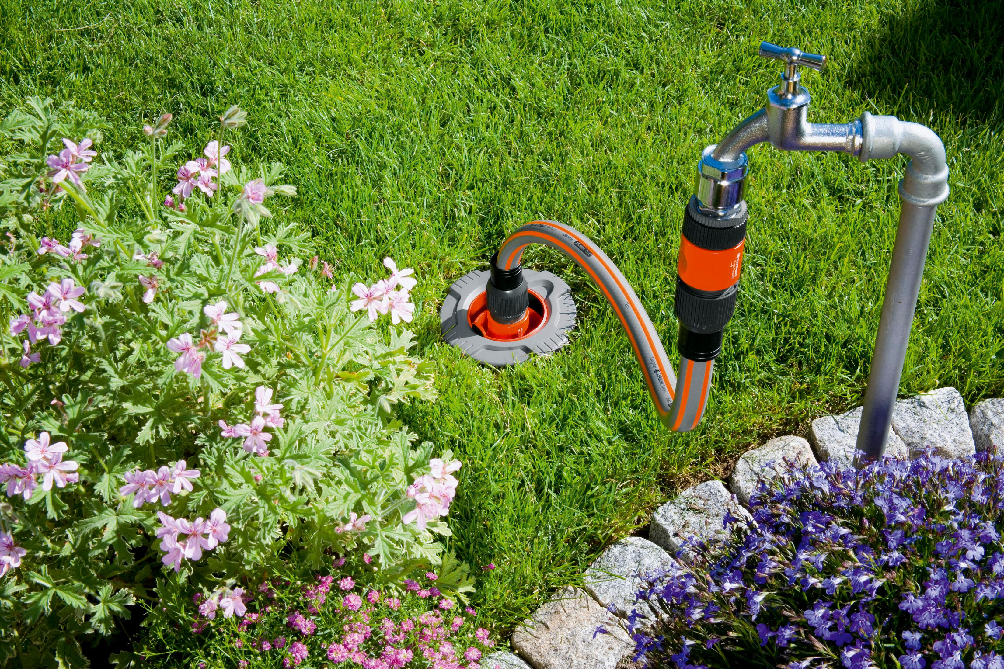 Ein Wasserhahn mit Schlauch auf einer Rasenfläche neben Blumen.