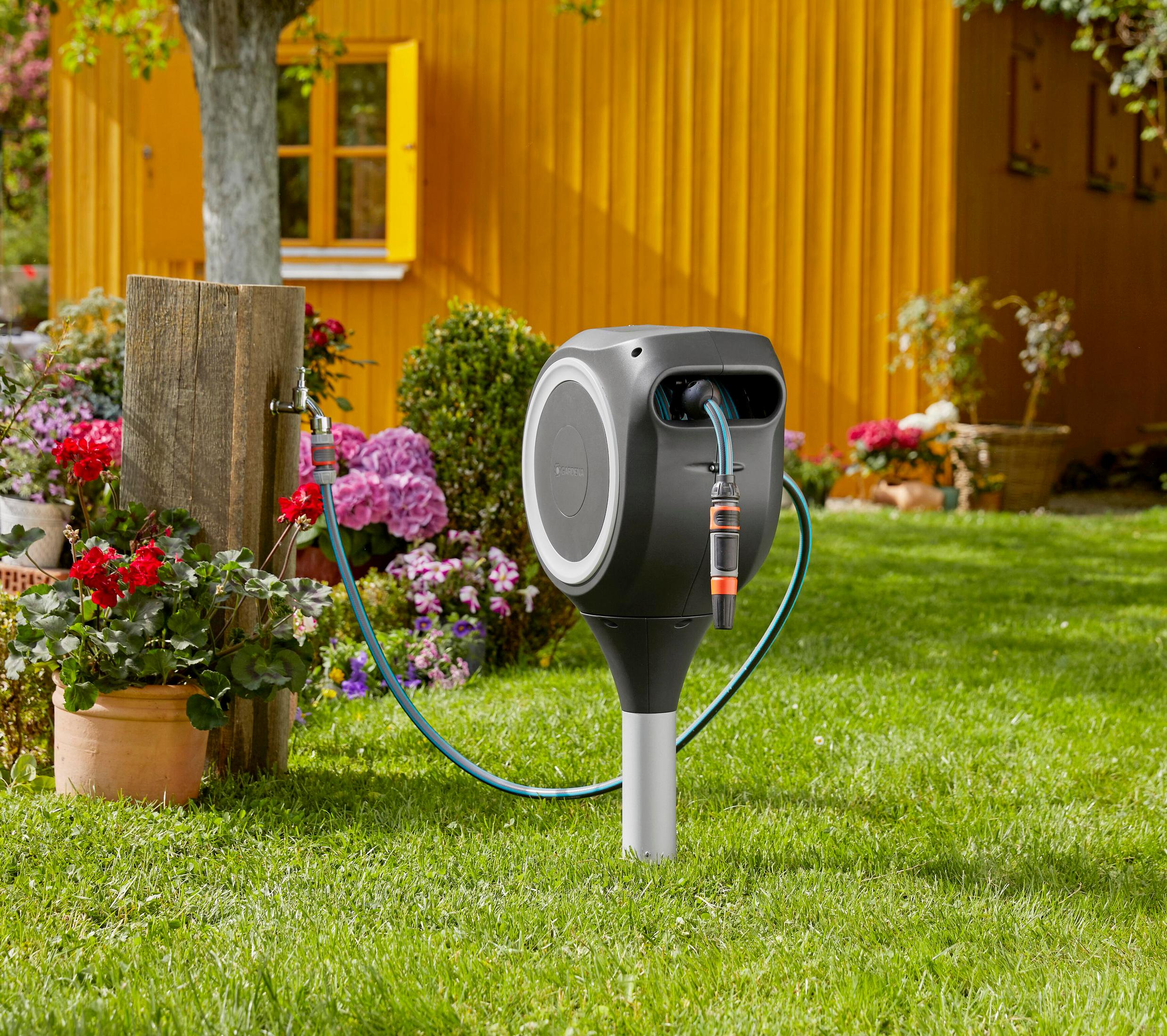 Ein automatischer Gartenschlauchaufroller steht im Gras vor einem gelben Haus.