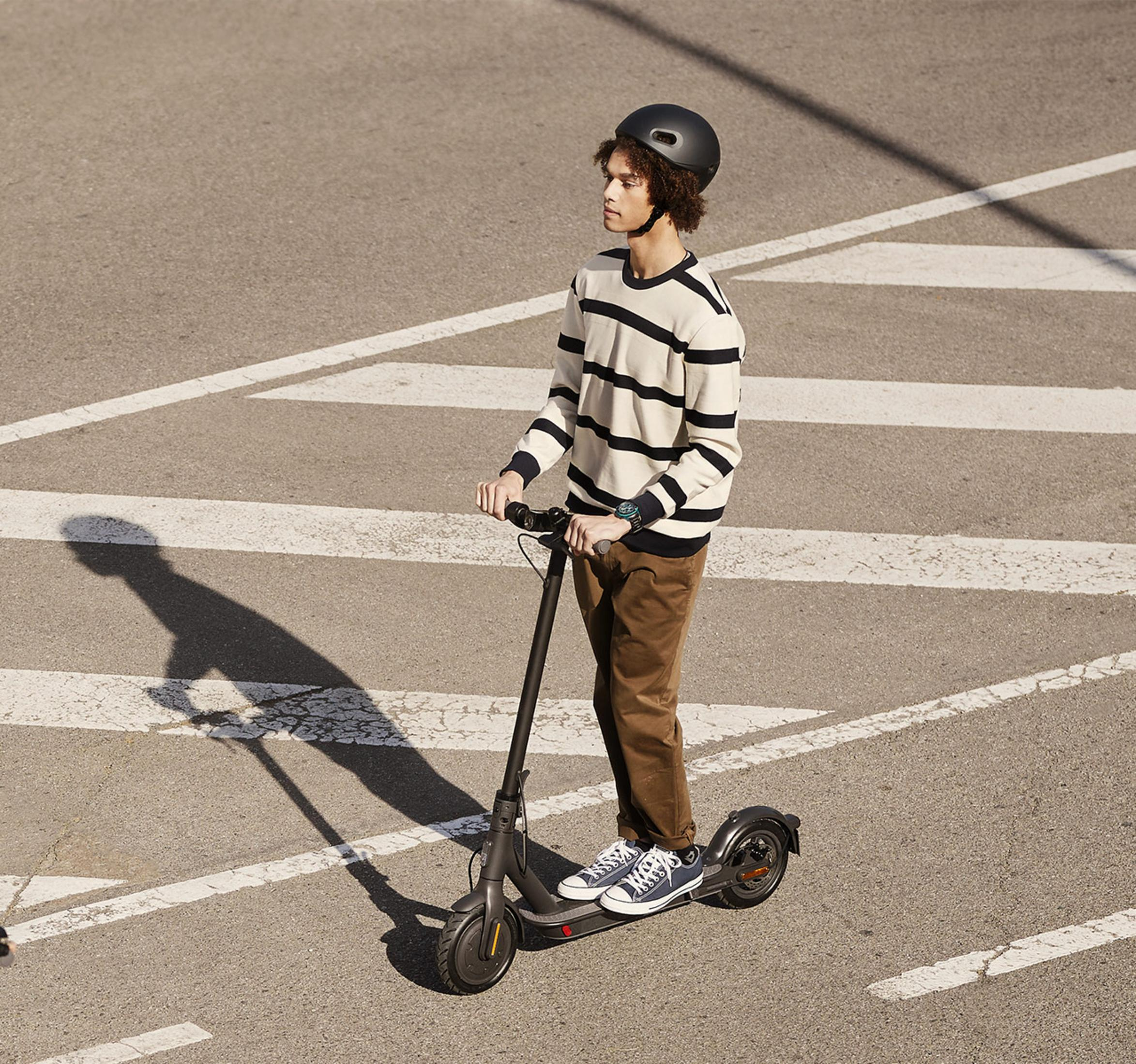 Un giovane con casco guida uno scooter elettrico su una strada con linee bianche.
