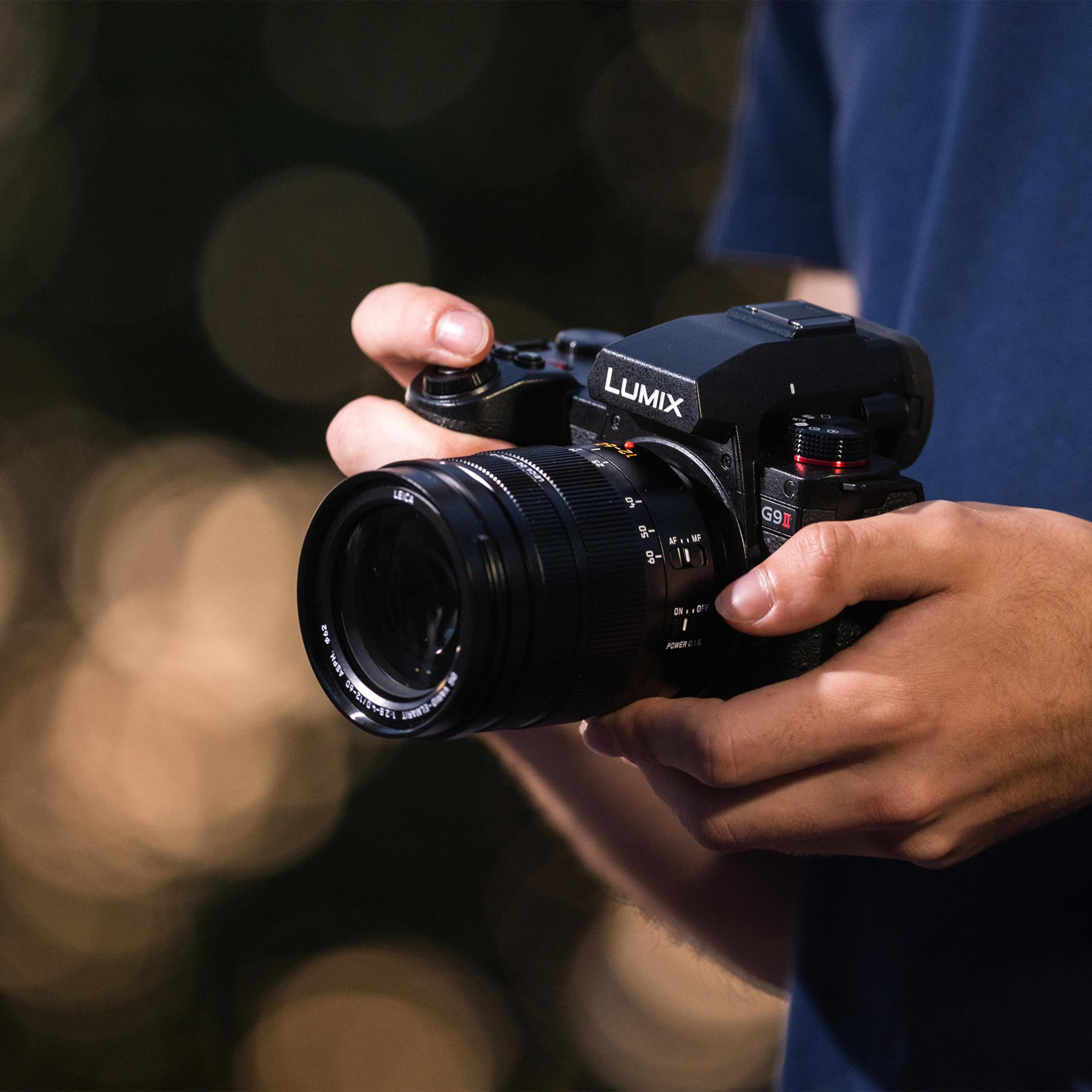 Hände halten eine schwarze Lumix G9II Kamera mit einem Leica Objektiv.