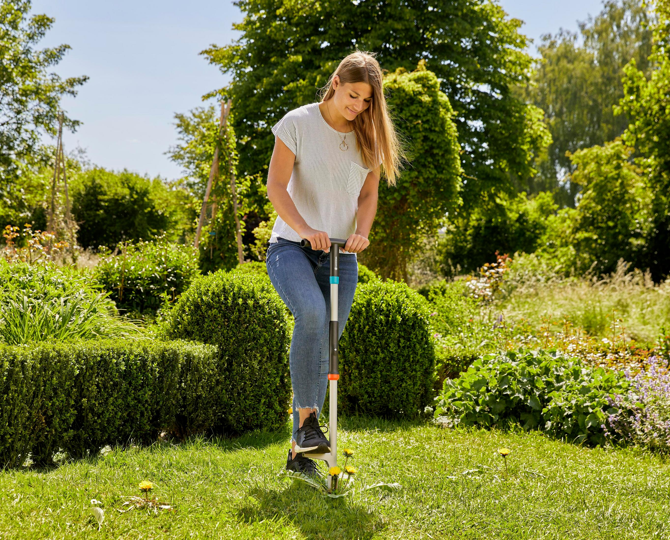 Donna usa uno strumento per estirpare erbacce in giardino.