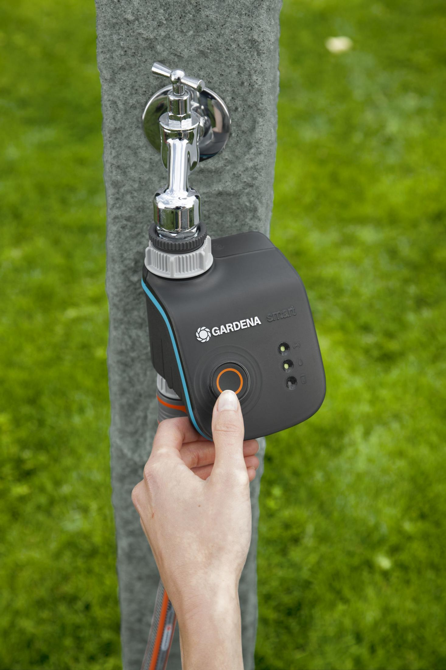 Un dito preme il pulsante di un computer per irrigazione Gardena Smart nero sul rubinetto.