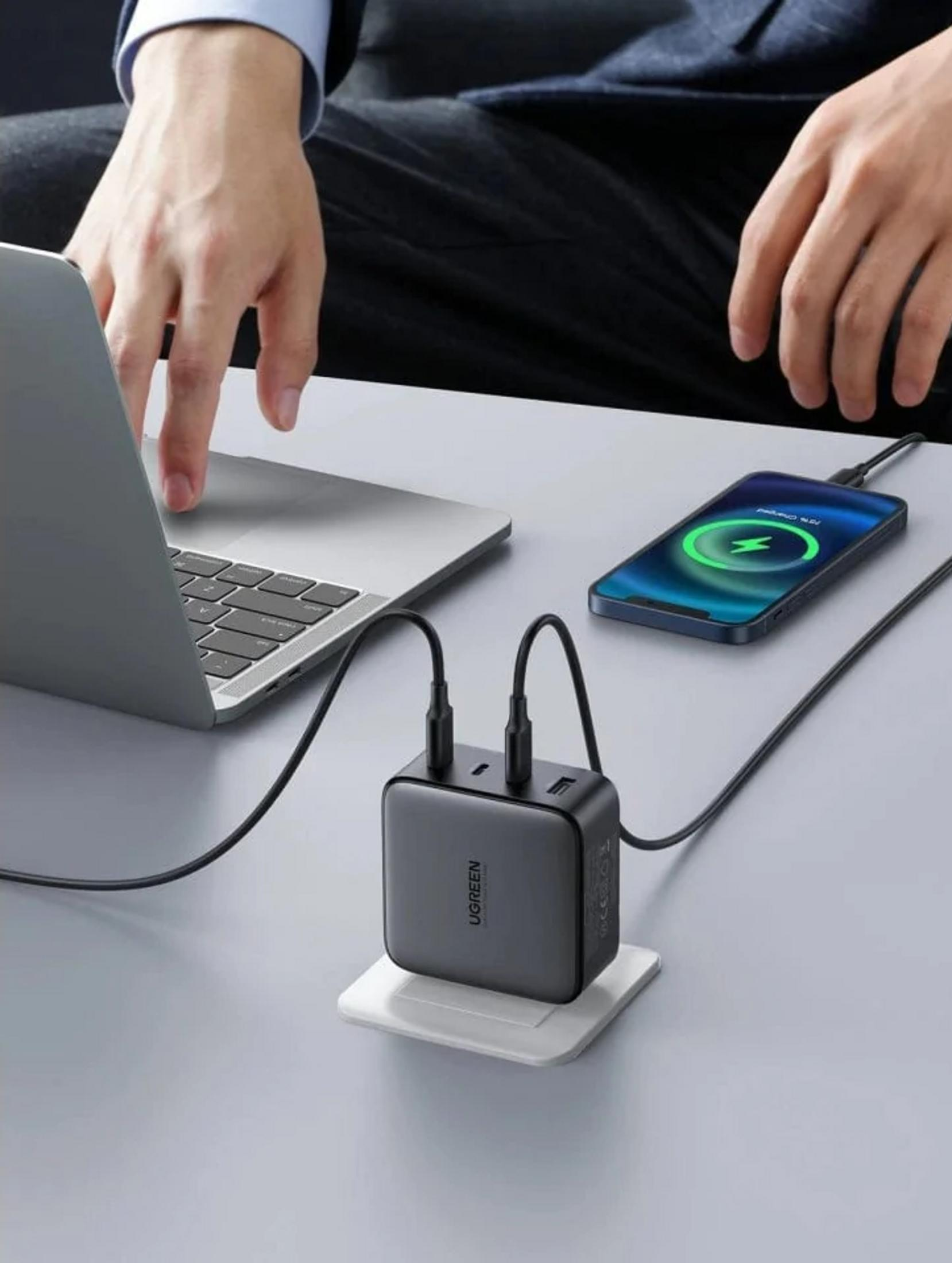 Ein Mann tippt auf einem Laptop, während ein Smartphone und ein Ladegerät angeschlossen sind.