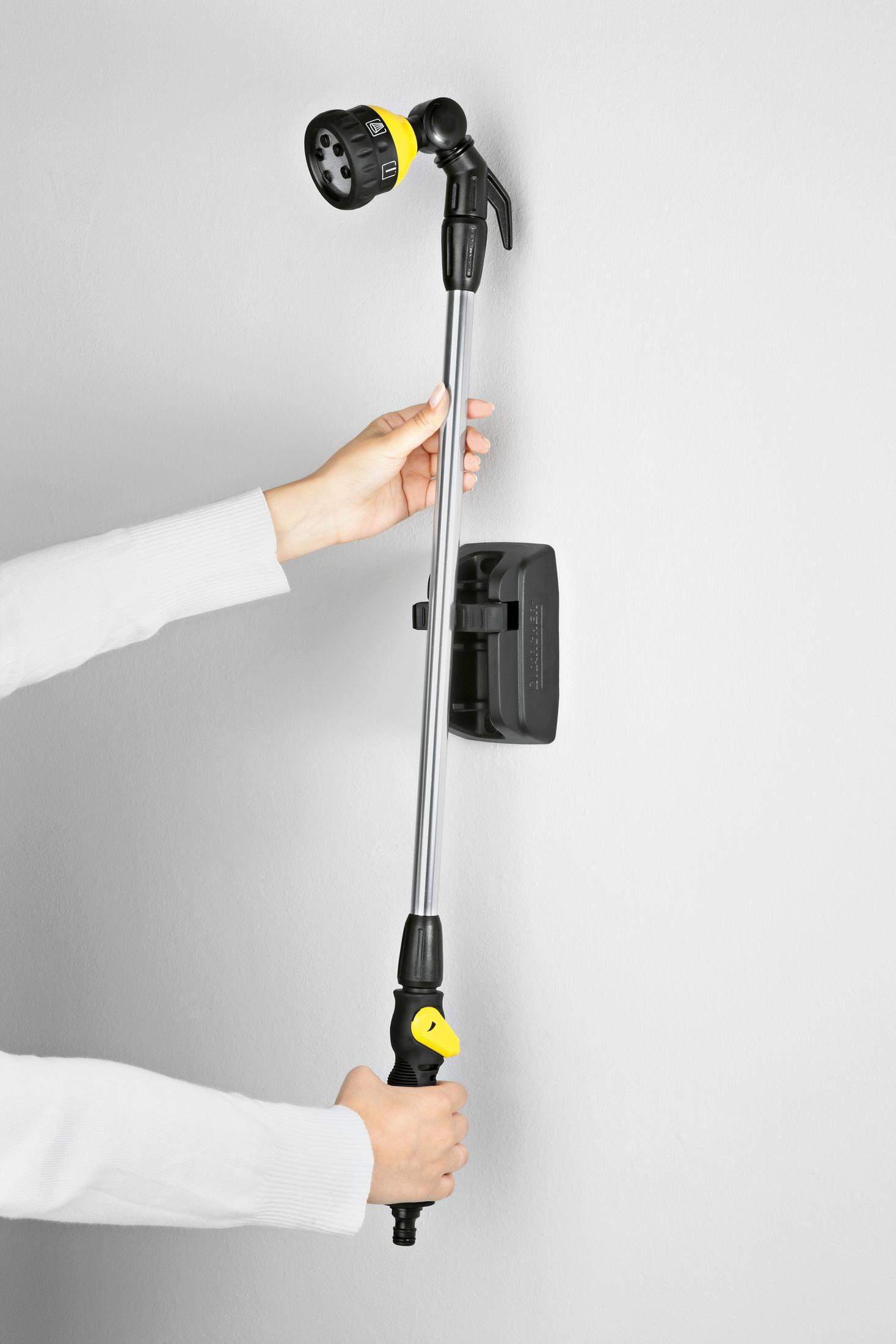 Eine Hand hält einen Teleskop-Duschkopf mit gelbem Griff an einer Wand.