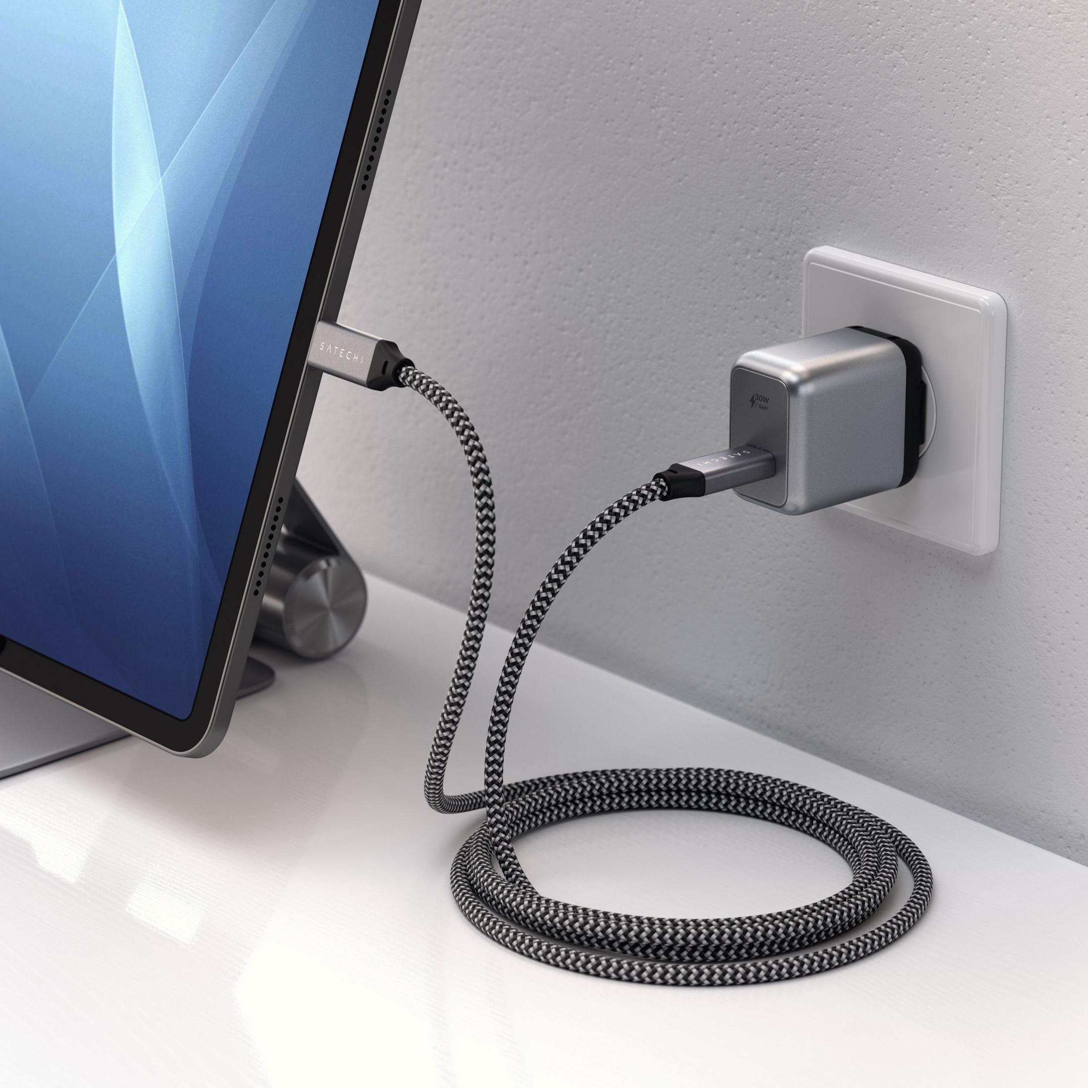Un tablet si sta caricando tramite un cavo collegato a un alimentatore inserito in una presa a muro.