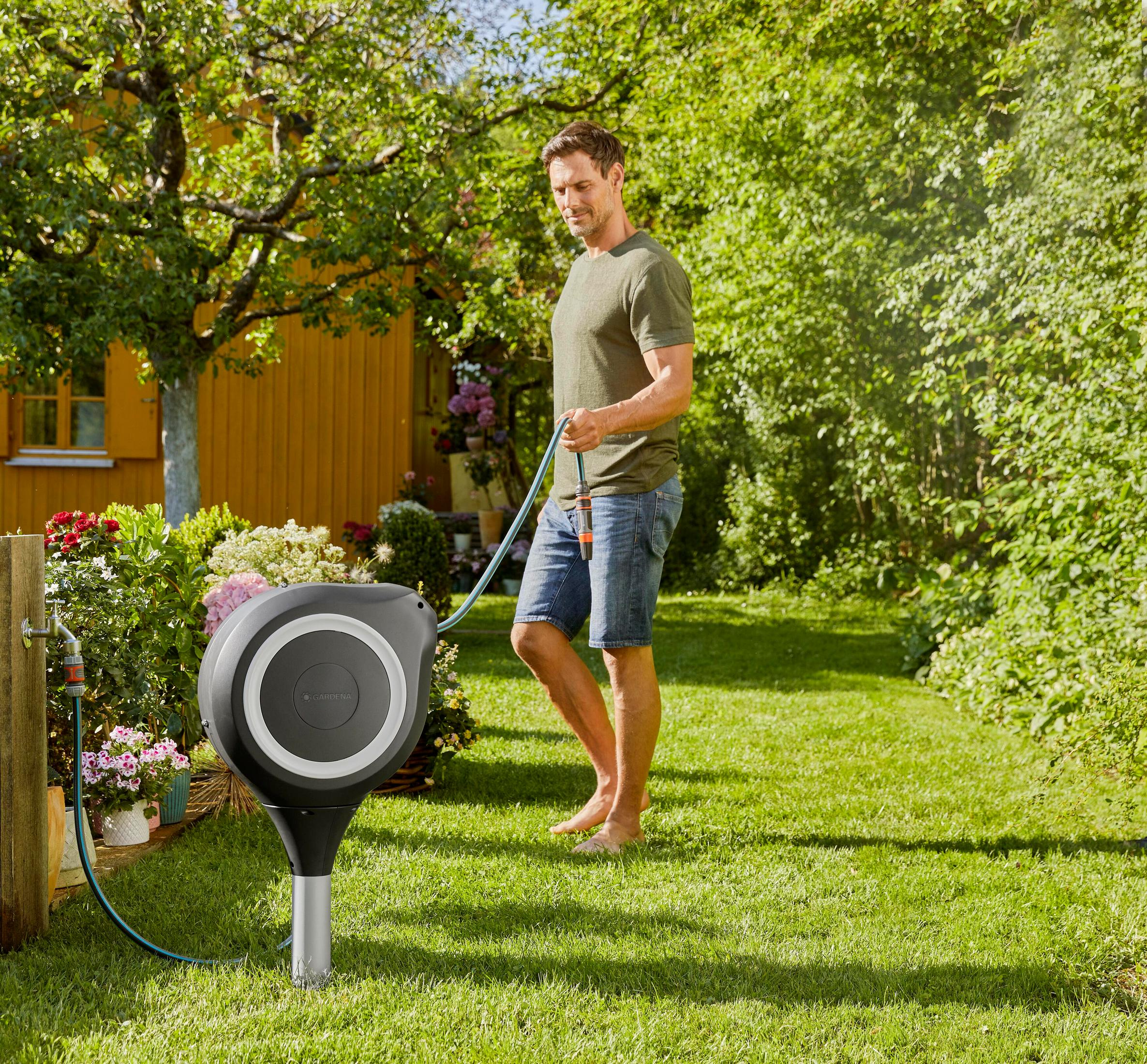 Uomo in giardino con tubo dell'acqua vicino all'avvolgitubo.