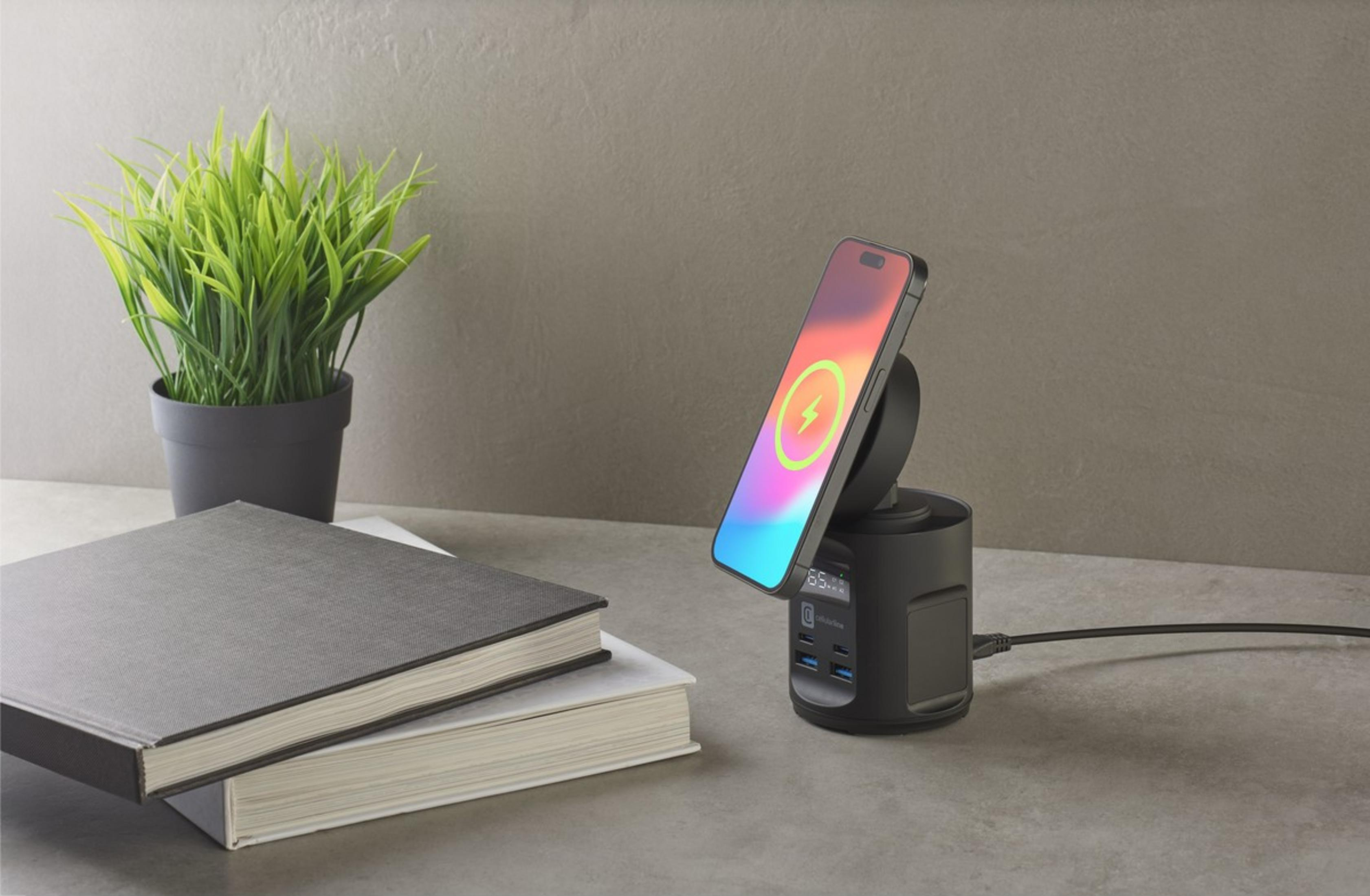 Ein Smartphone lädt auf einem schwarzen Ständer neben Büchern und einer Pflanze.