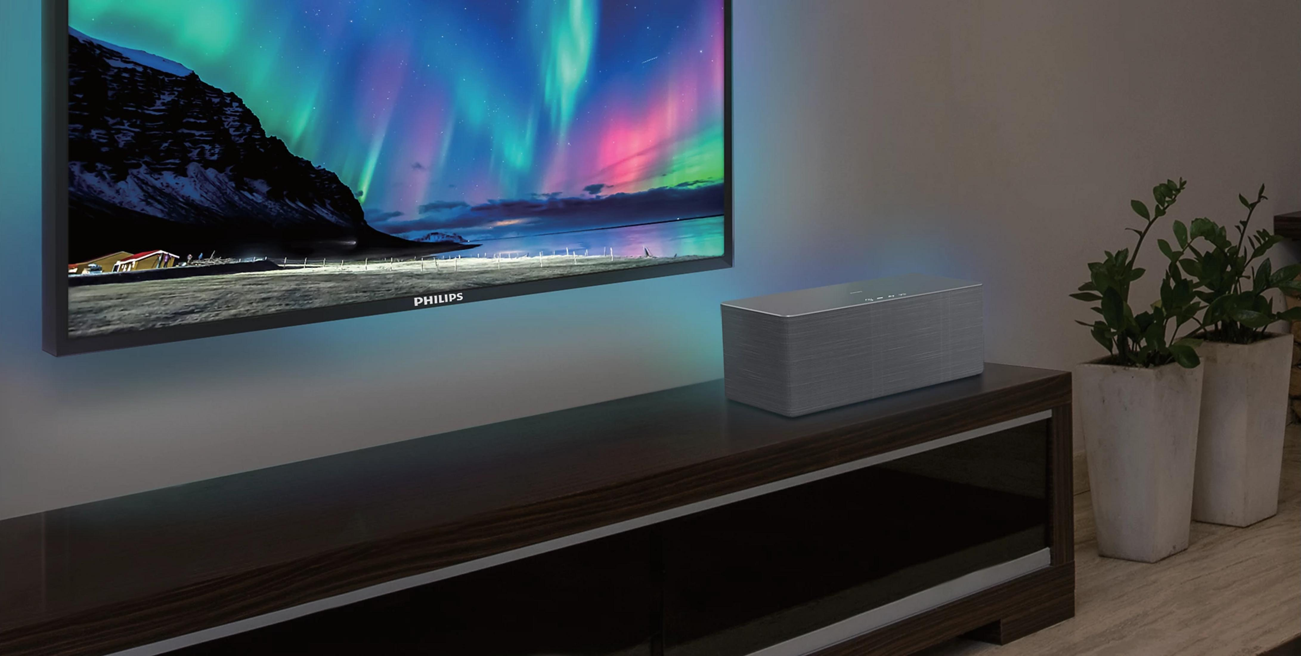 Une grande enceinte grise est posée sur un meuble TV sombre.