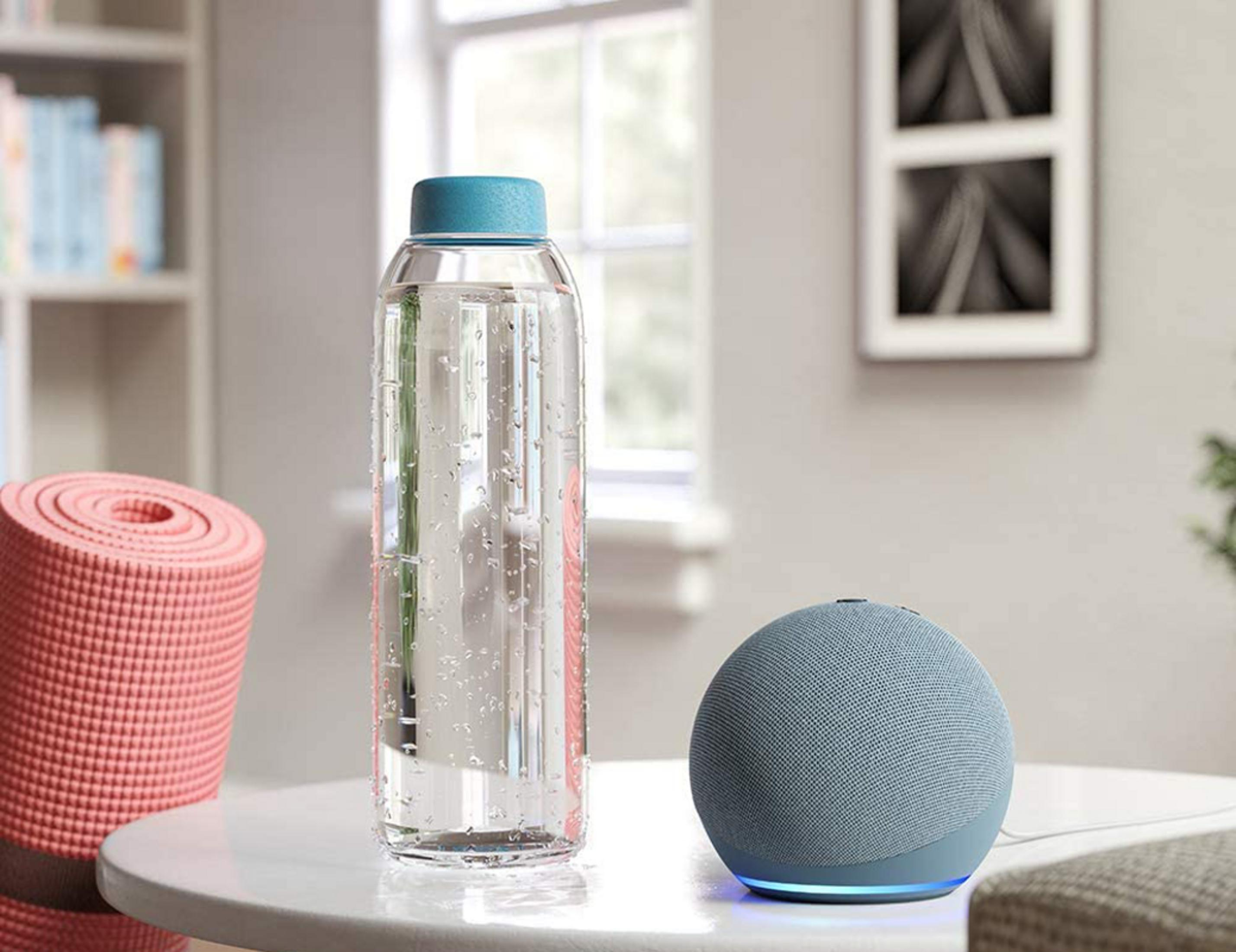Ein blauer Smart Speaker steht neben einer Wasserflasche und einer rosa Yogamatte.