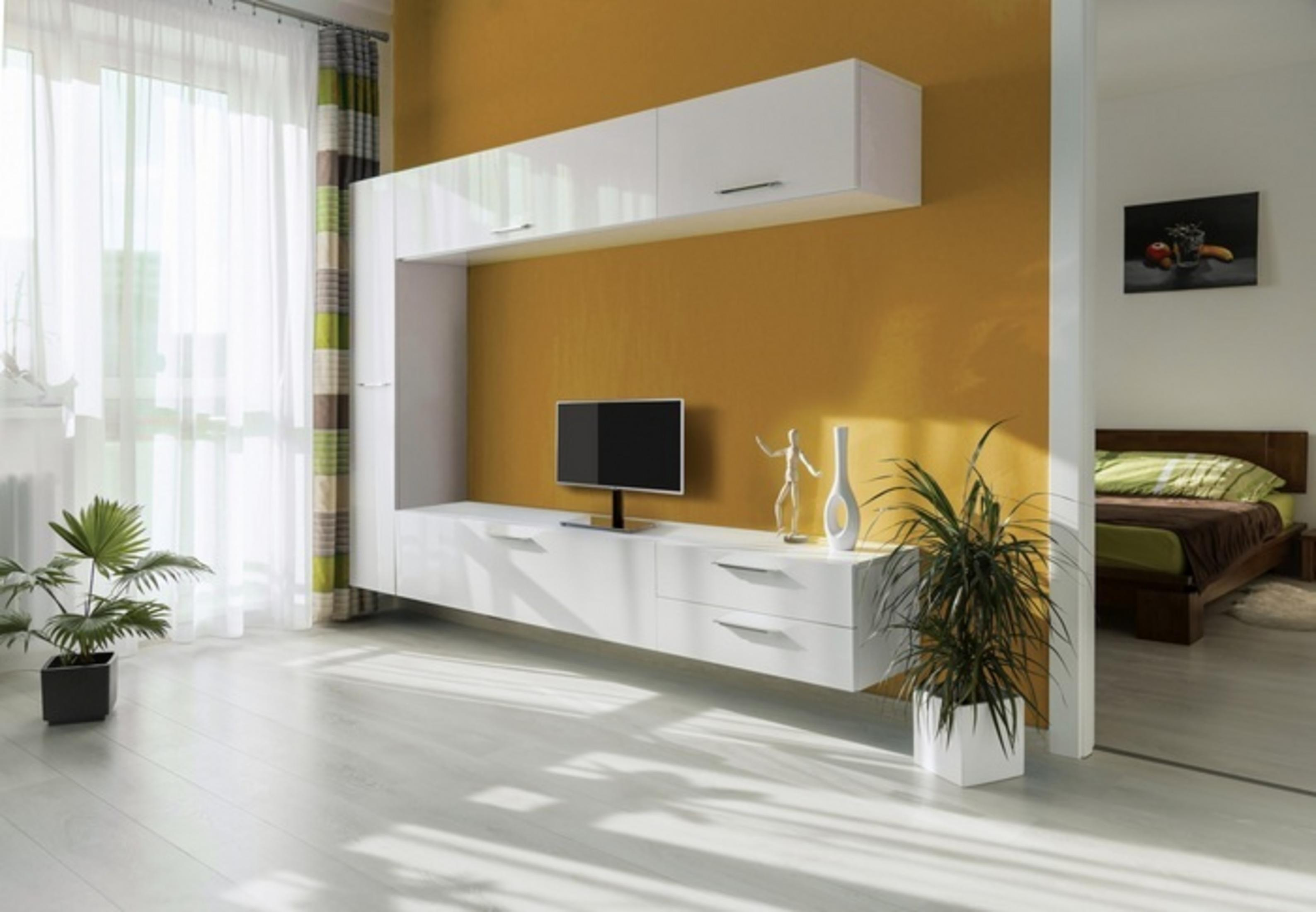 Modernes Wohnzimmer mit gelber Wand, weißem TV-Möbel, Pflanzen und Bett.