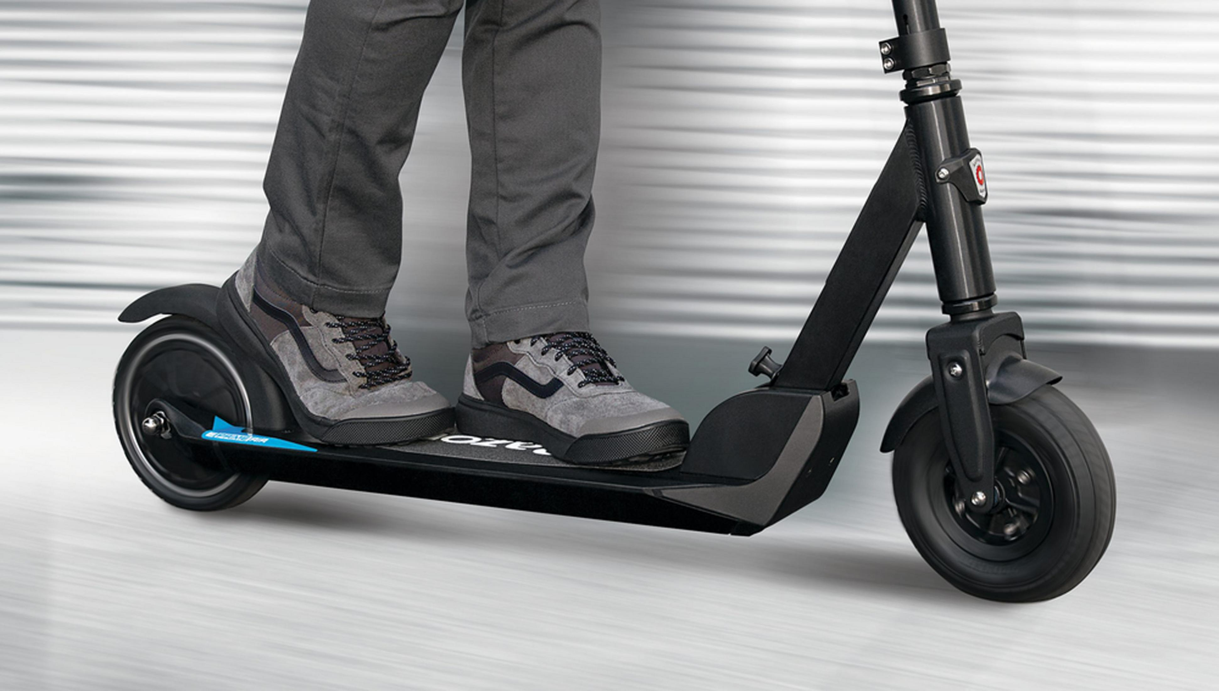 Pantaloni grigi e scarpe da ginnastica su e-scooter nero con sfondo argento.