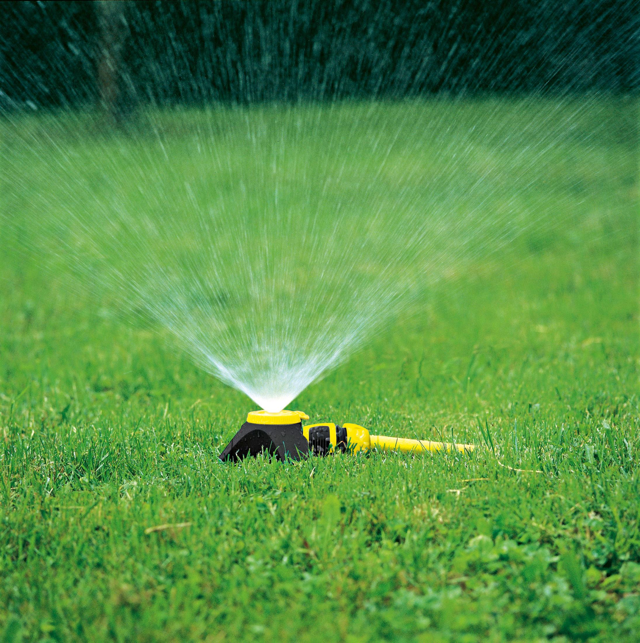Ein gelber Gartenschlauchsprinkler bewässert grünes Gras mit feinen Wasserstrahlen.