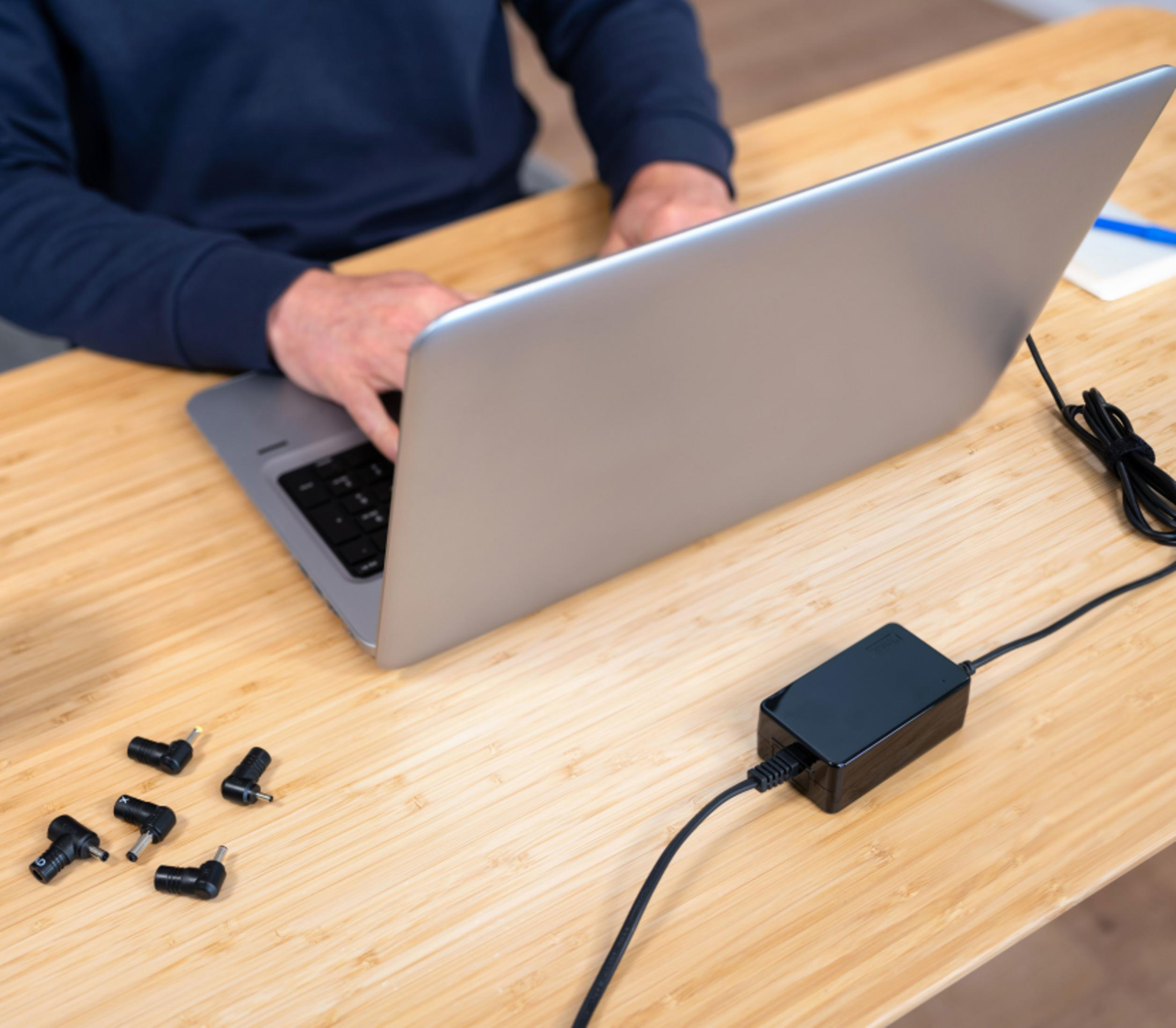 Un adaptador de corriente para portátil con varias puntas sobre un escritorio de madera.