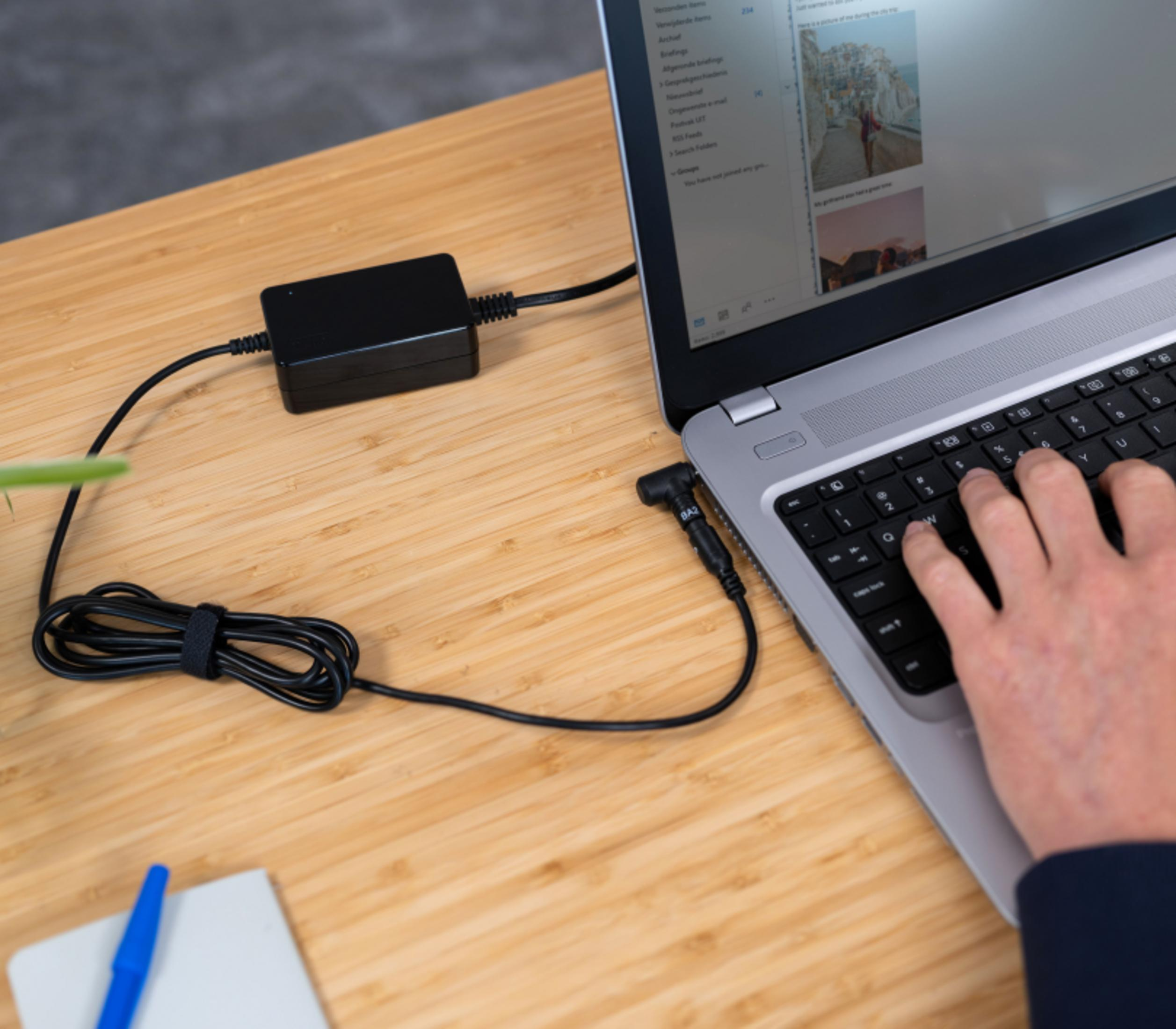 Ein Laptop ist über ein Netzteil mit Strom versorgt. Eine Hand tippt auf der Tastatur.