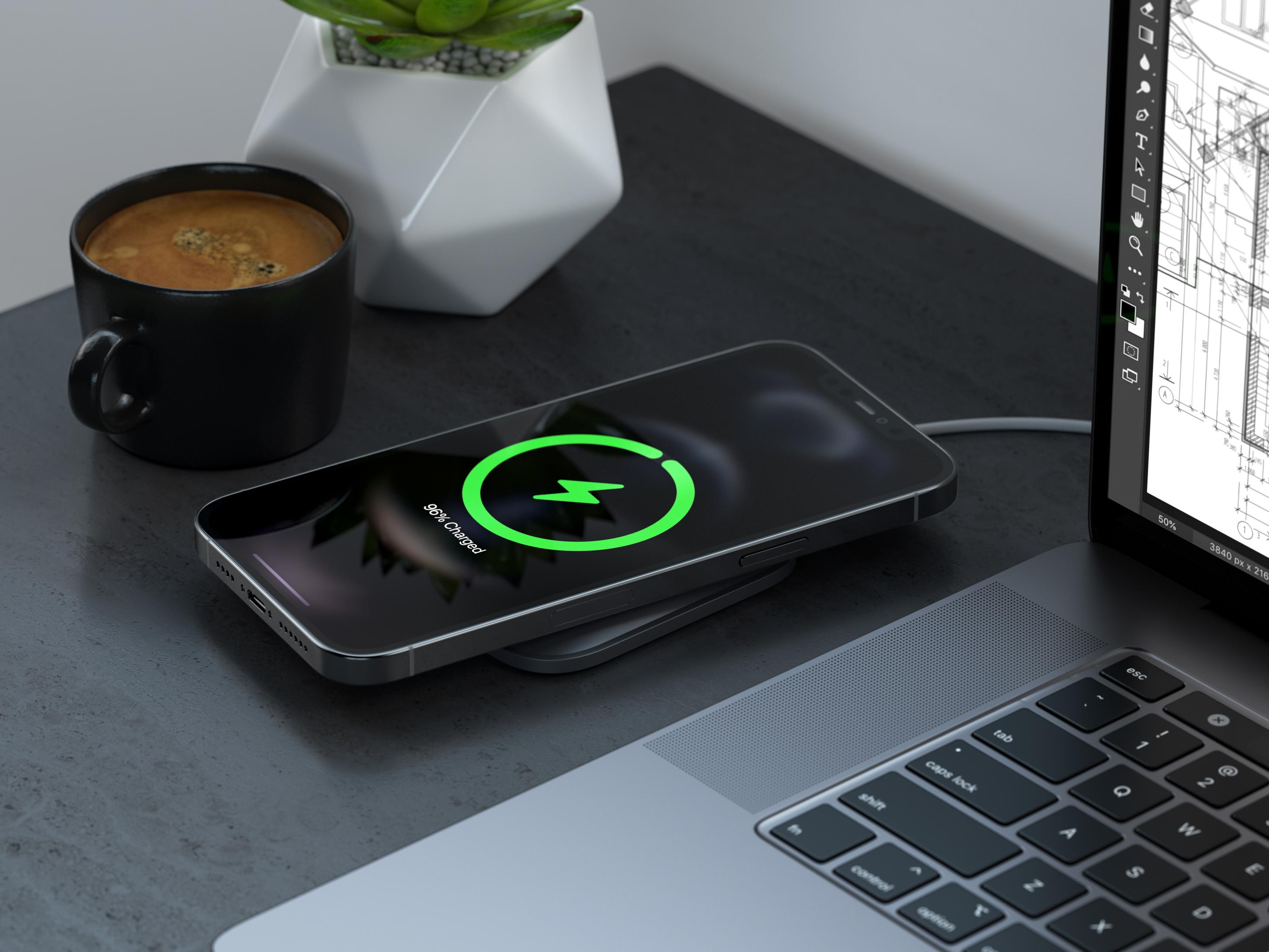 Ein Smartphone wird kabellos auf einem Laptop geladen, daneben eine Tasse Kaffee.