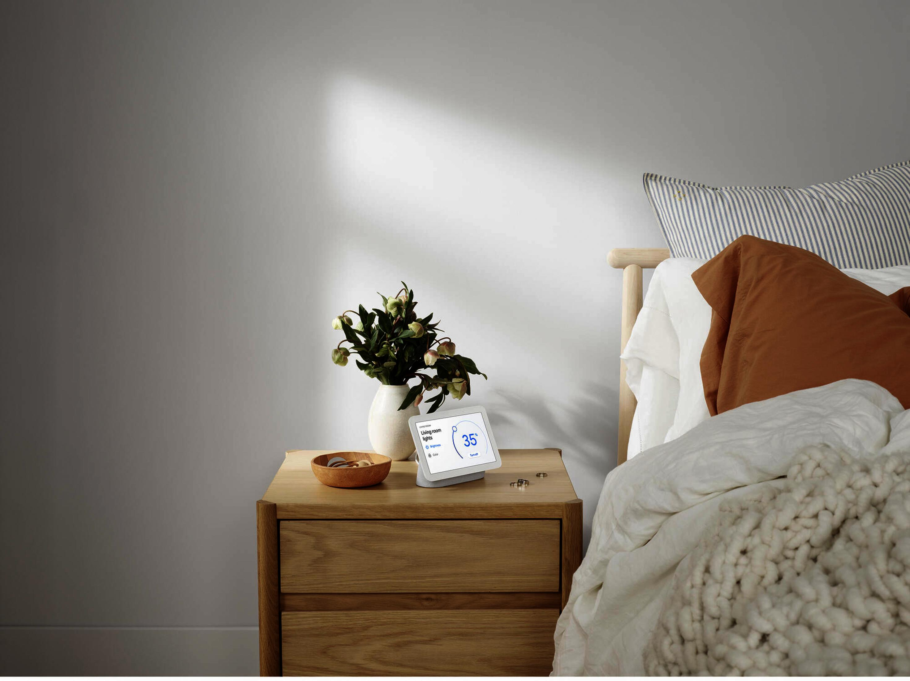Un comodino accanto a un letto con fiori in vaso e un display intelligente.
