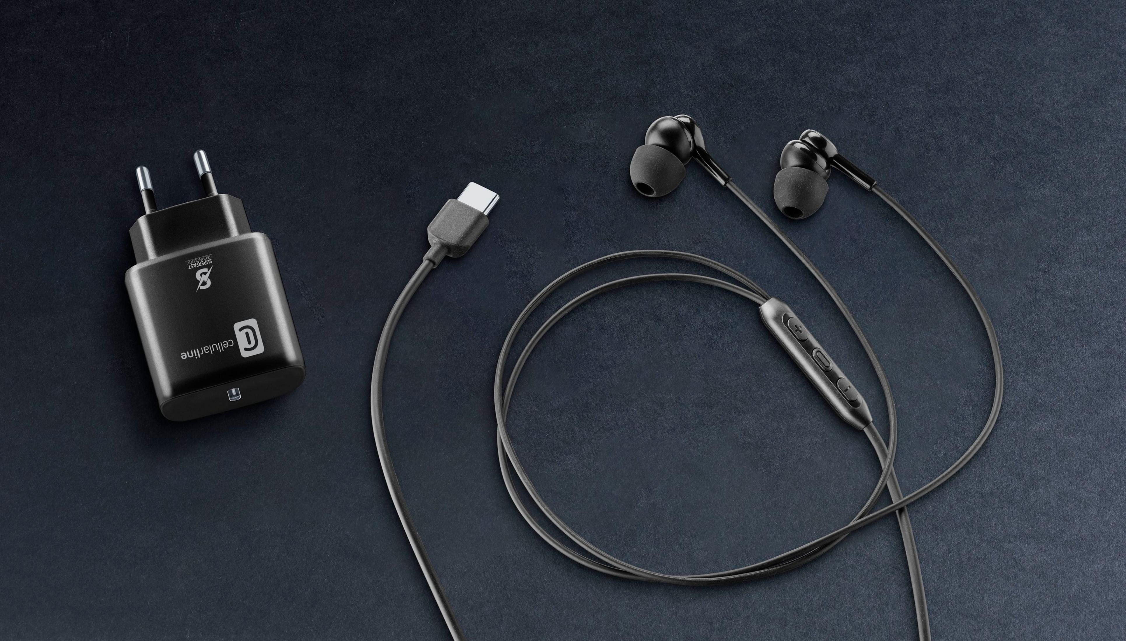 Cargador negro con cable USB-C y auriculares in-ear sobre fondo oscuro.