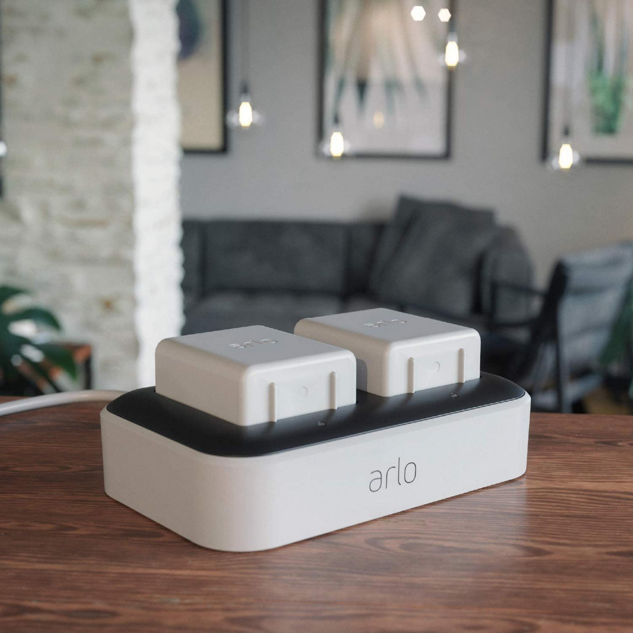 Ein weißes Arlo Ladegerät mit zwei Kameras steht auf einem Holztisch.