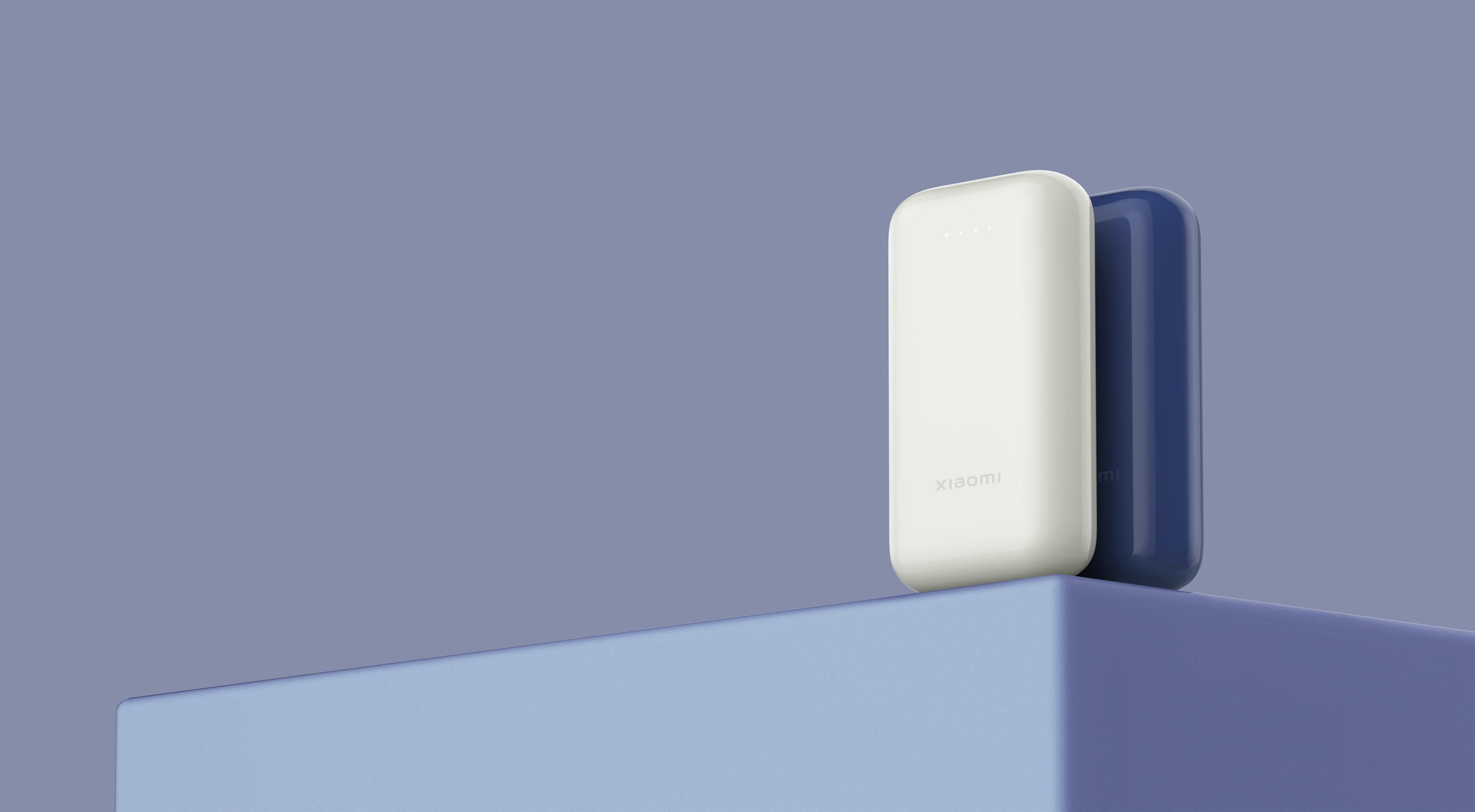 Twee Xiaomi powerbanks, wit en blauw, op een blauw podium tegen paarse achtergrond.
