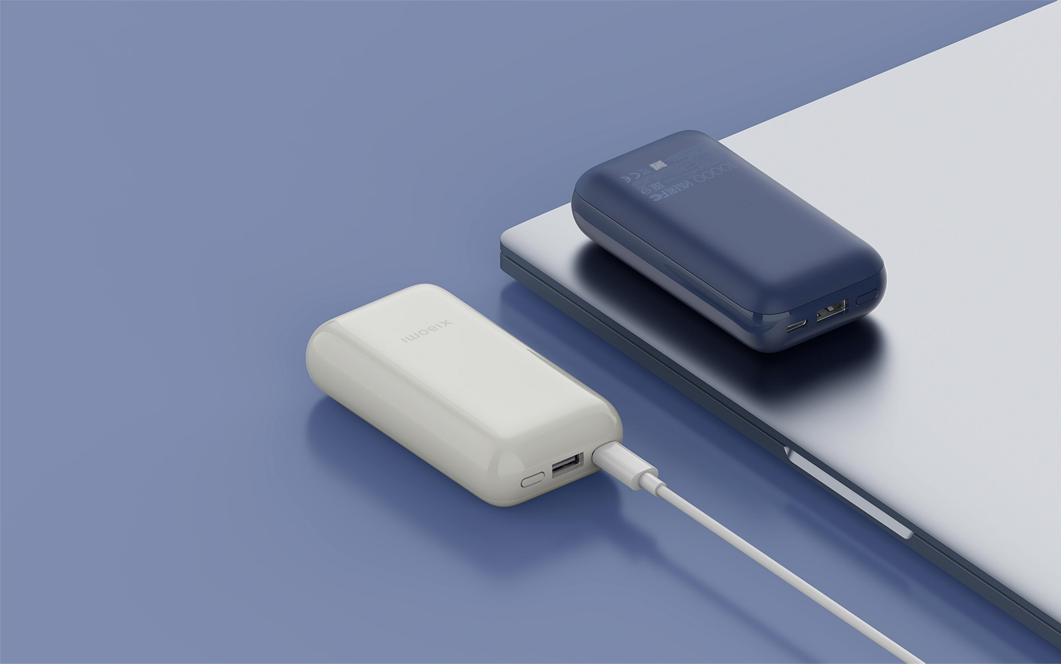 Twee powerbanks, wit en blauw, liggen op een laptop. Een kabel verbindt de witte.