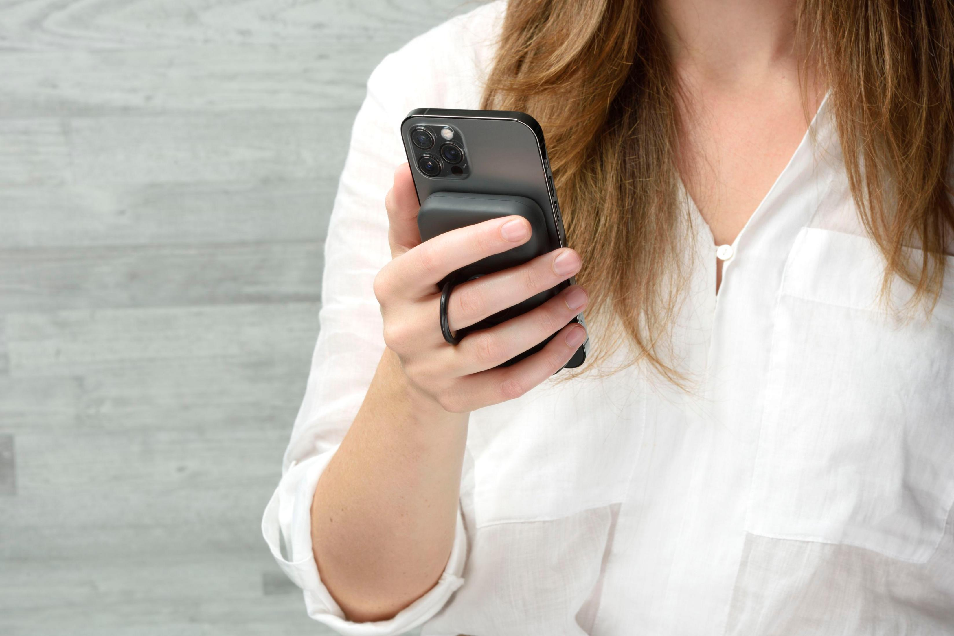 Una donna in camicia bianca tiene uno smartphone scuro con un anello porta telefono.