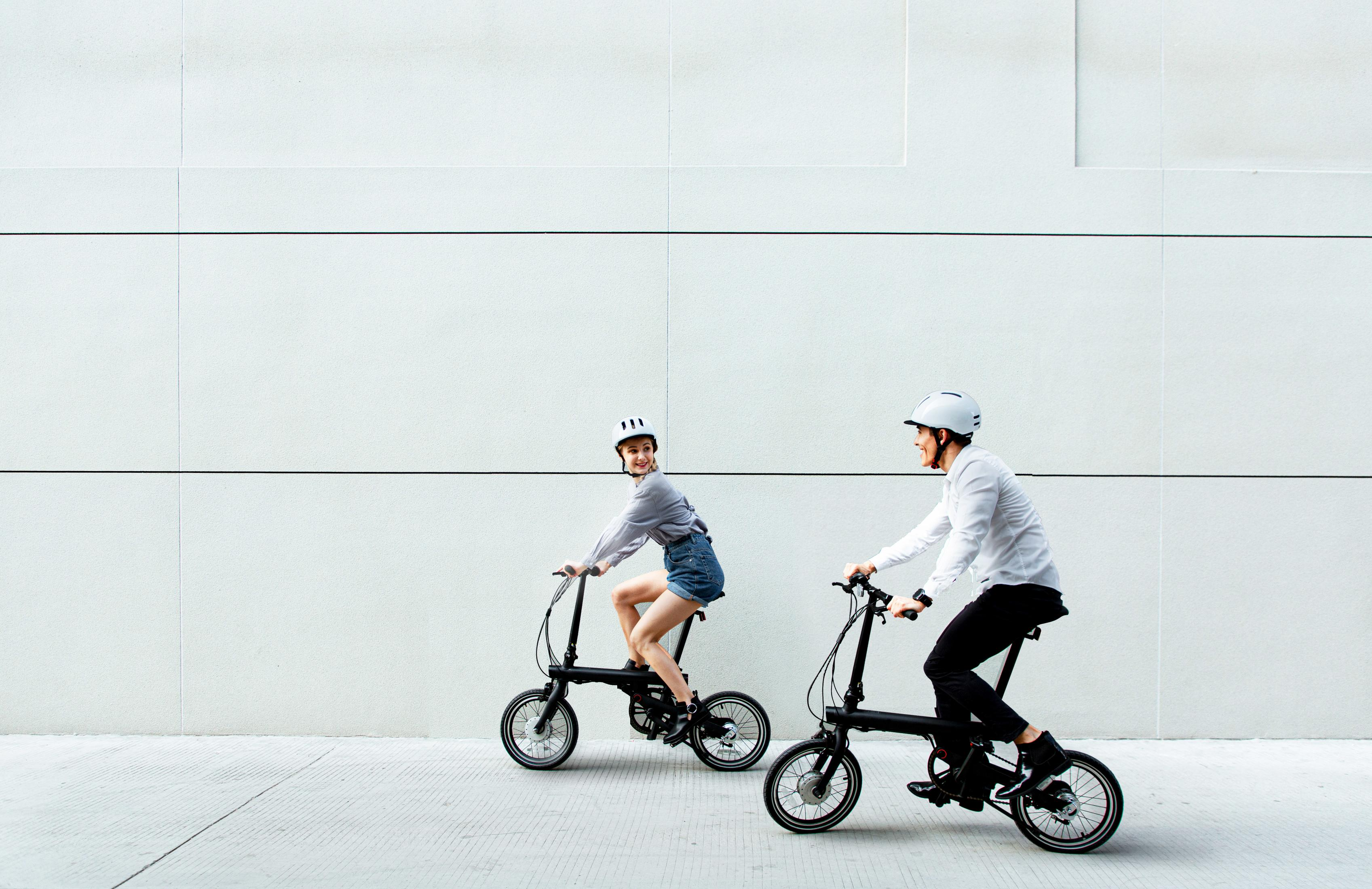 Uomo e donna in bicicletta pieghevole davanti a muro bianco.
