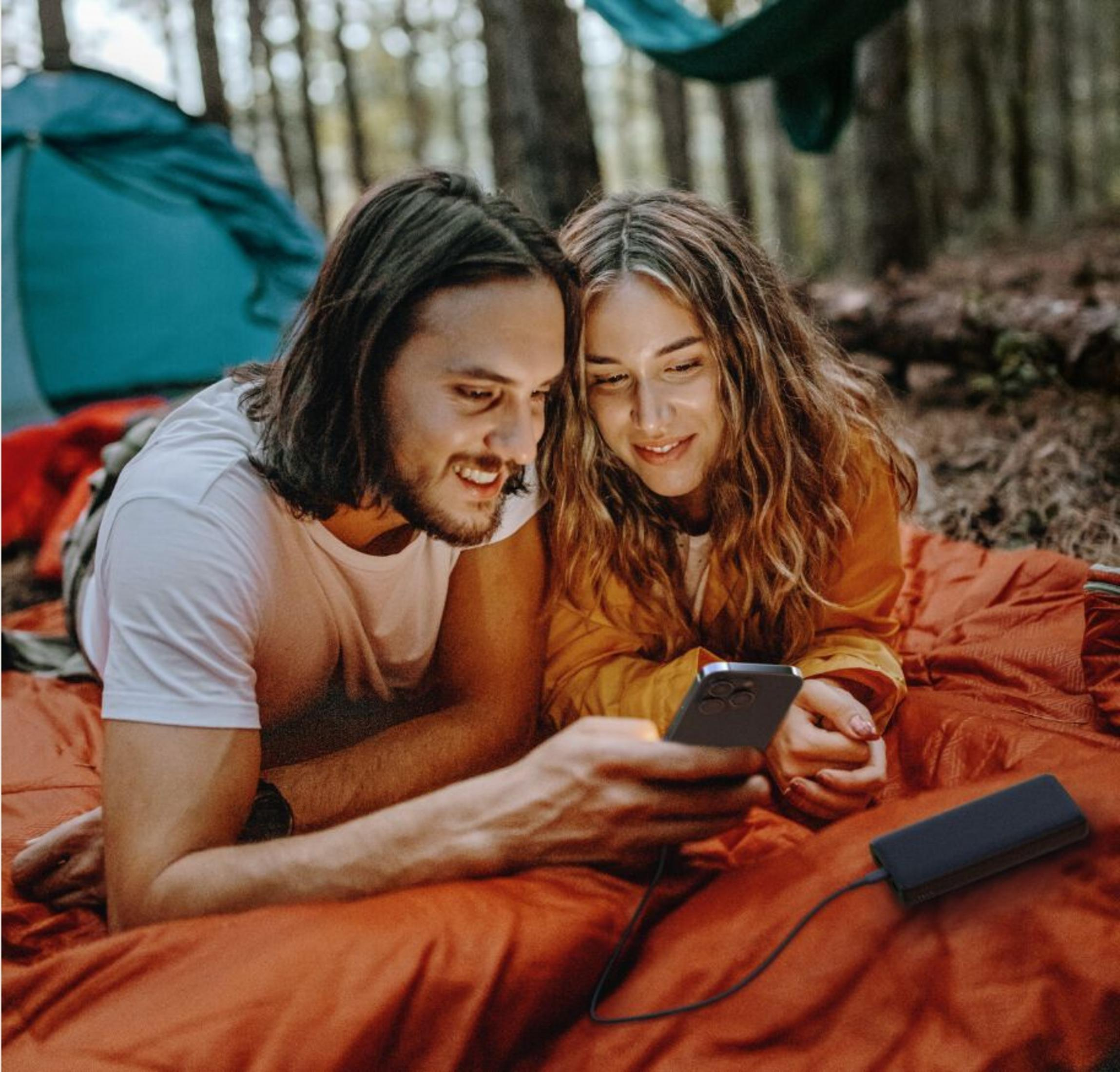 Una coppia giace su una coperta arancione nel bosco guardando un telefono.