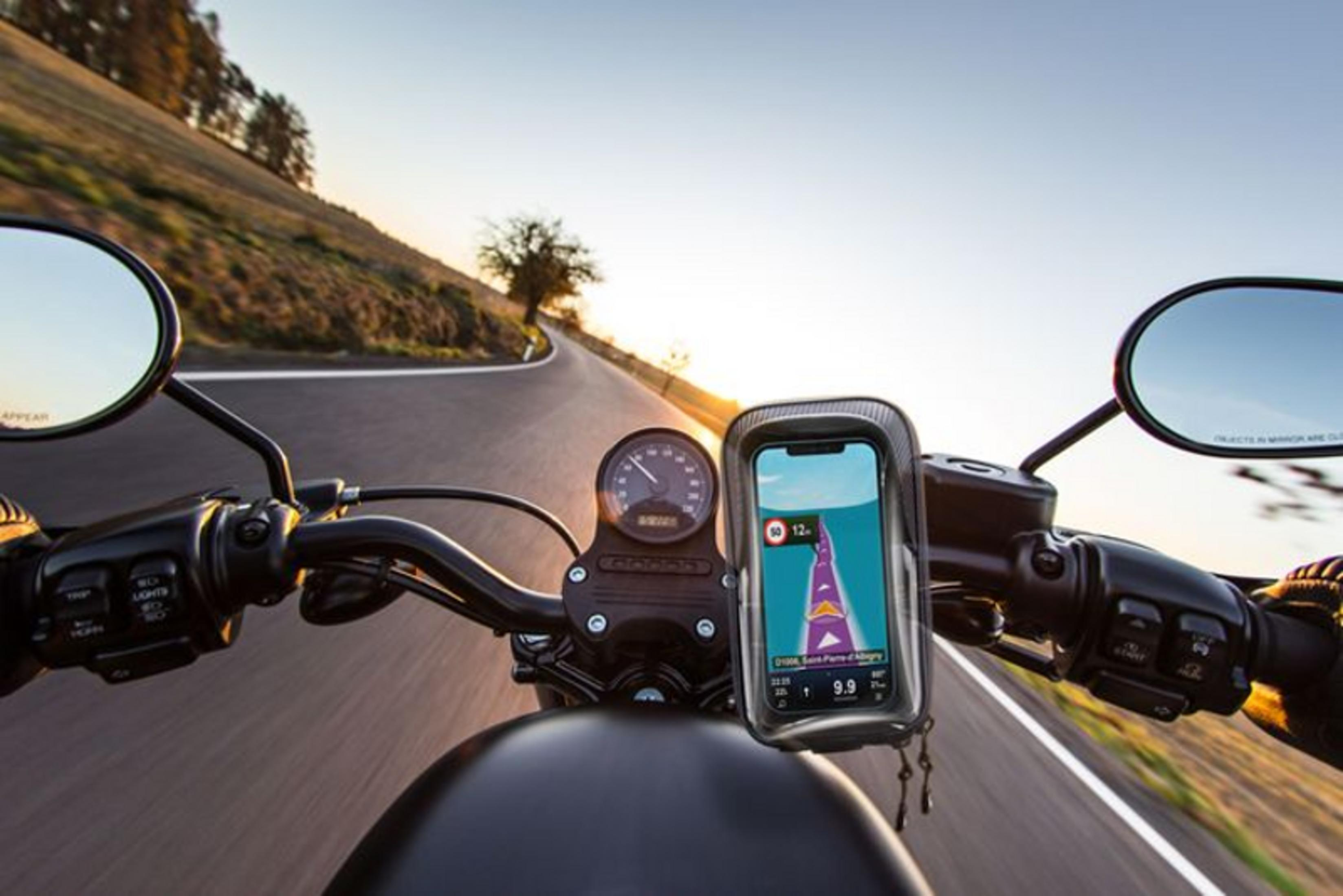 Motorfietsnavigatie op stuur, bochtige weg bij zonsondergang.