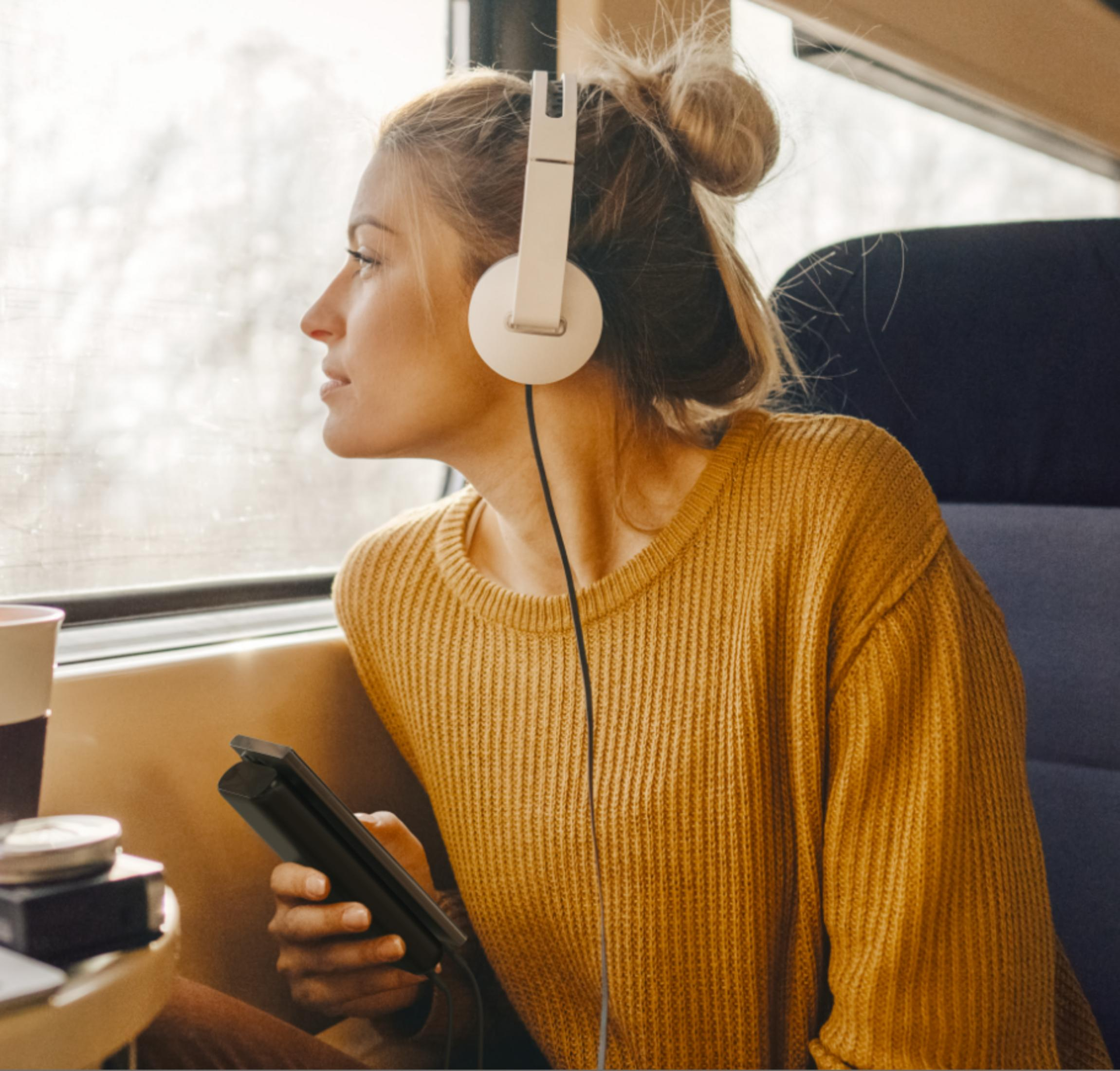 Donna con cuffie e telefono guarda fuori dal finestrino del treno.