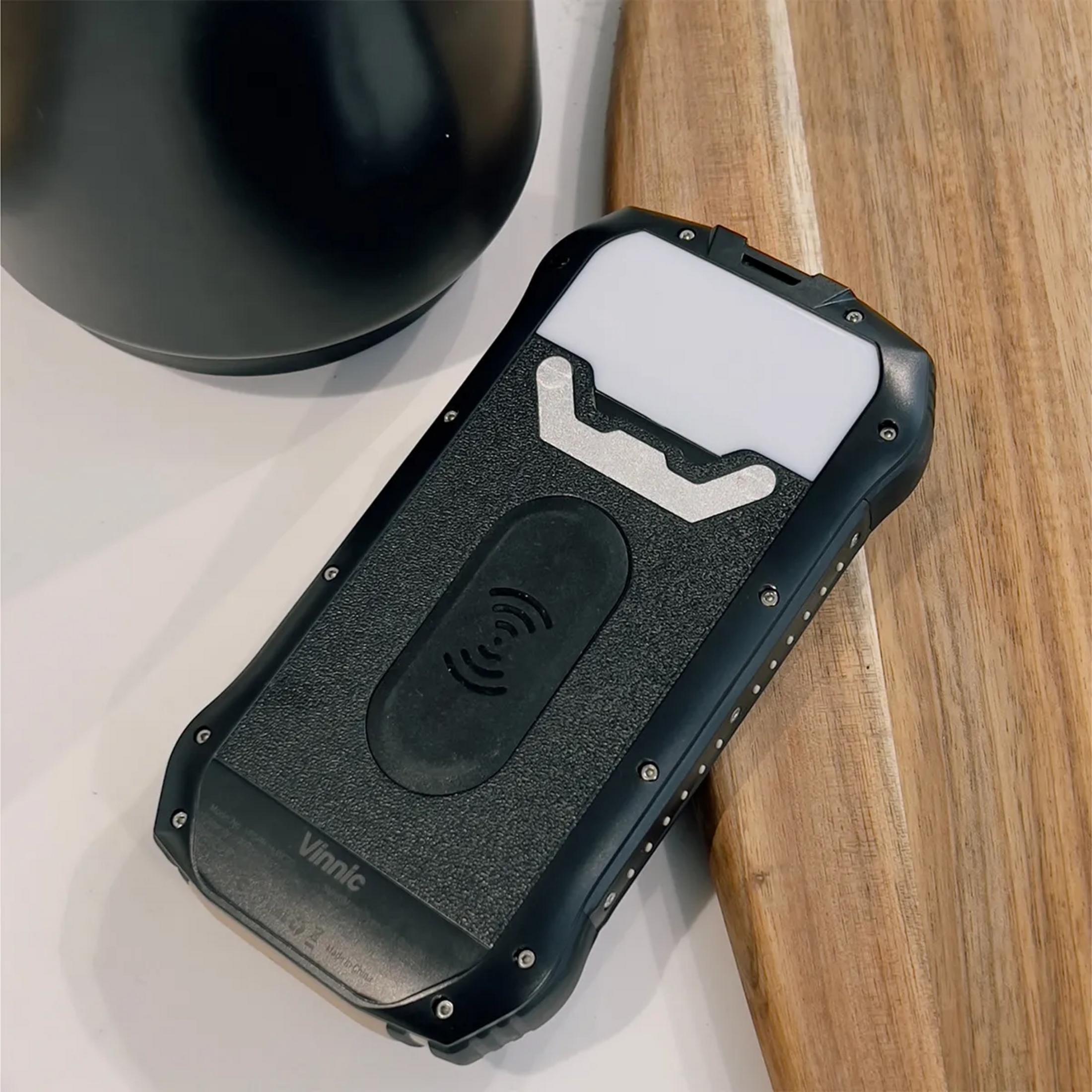 Téléphone robuste noir avec zone de recharge et lumière sur fond bois.
